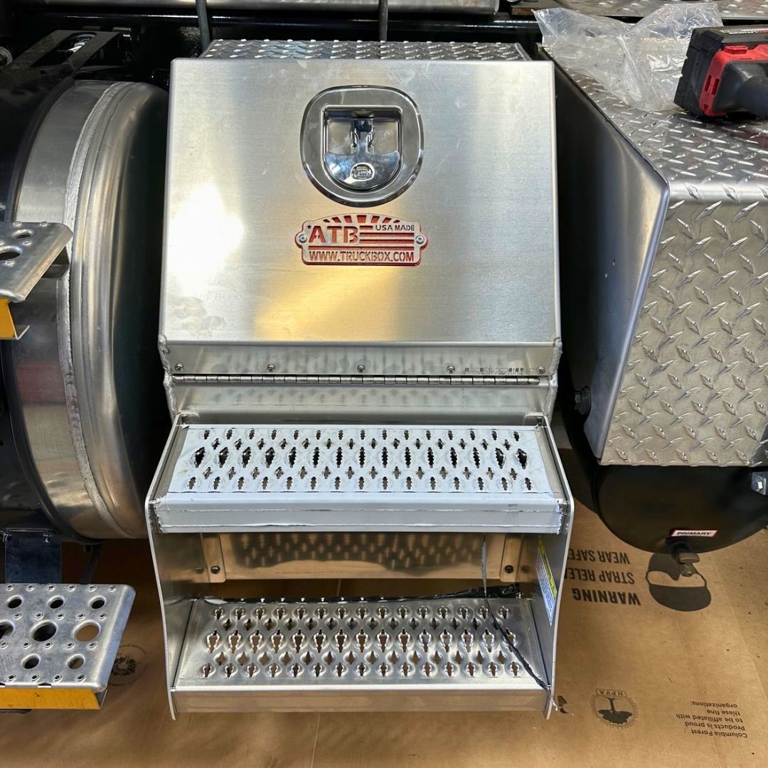 Silver truck toolbox with built-in steps, mounted on a semi-truck.