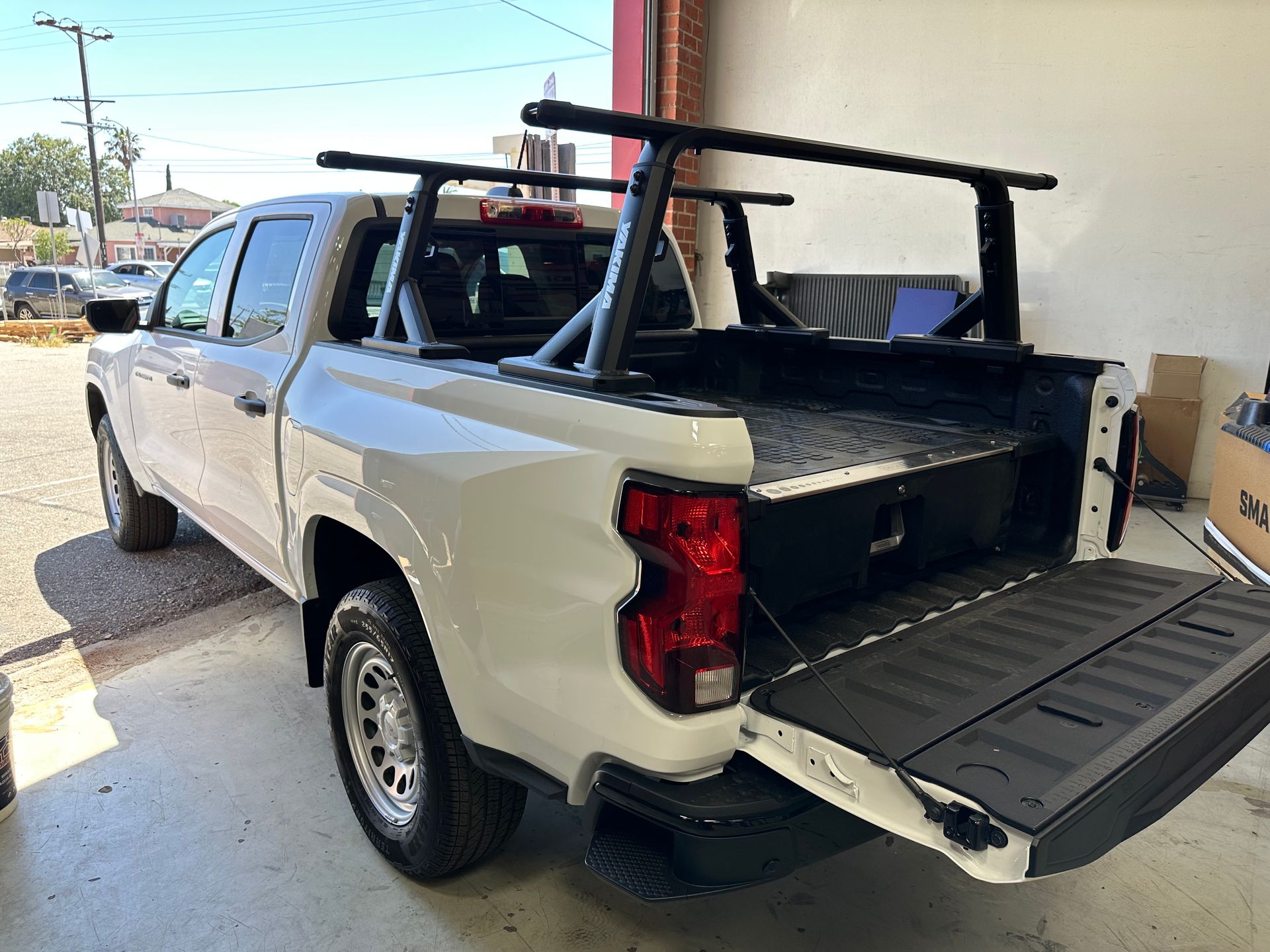 A white pickup truck with a black utility rack installed in the truck bed, parked with the tailgate open.