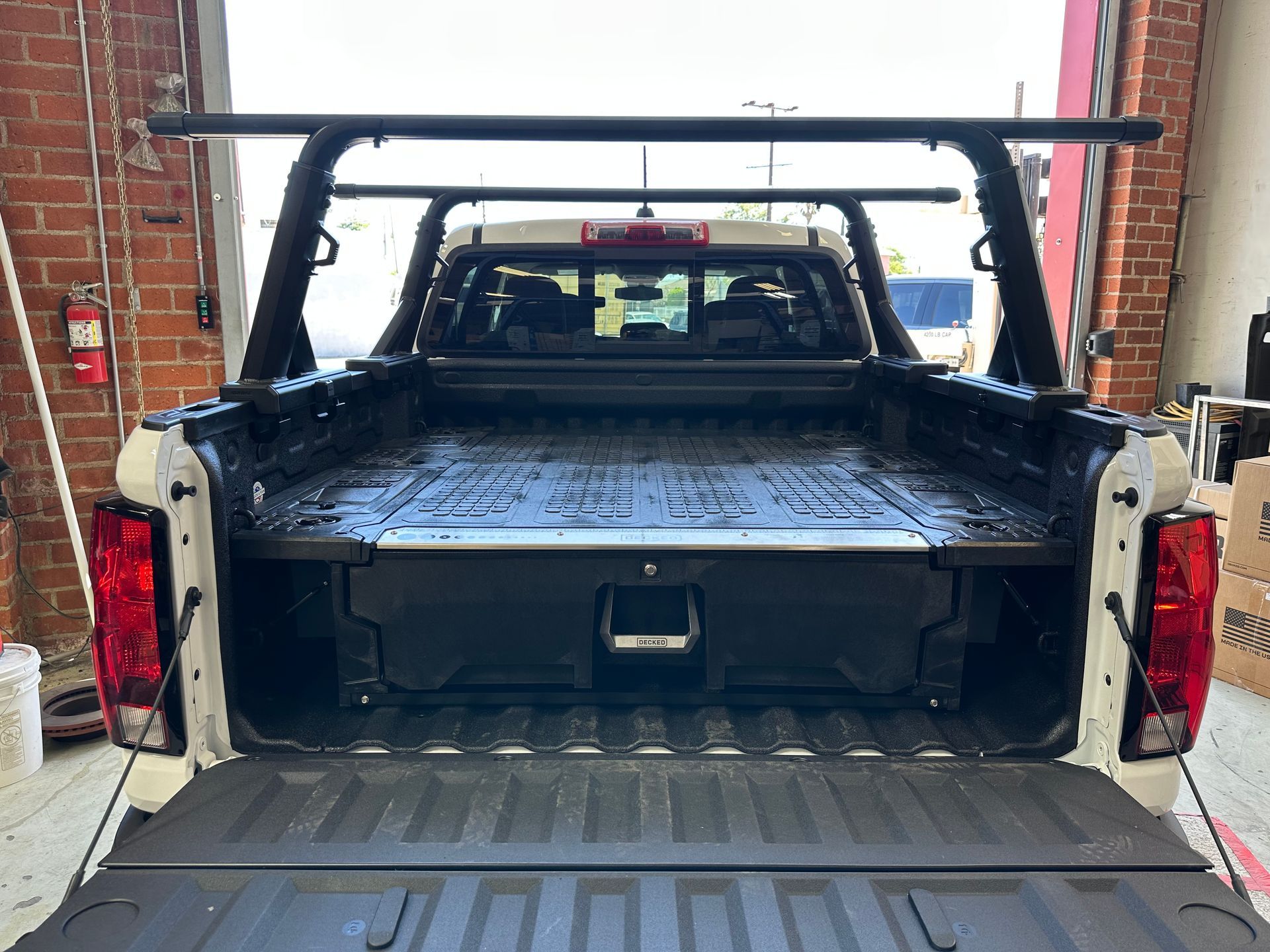 Rear view of a white pickup truck bed featuring a black integrated storage drawer system and a metal ladder rack.