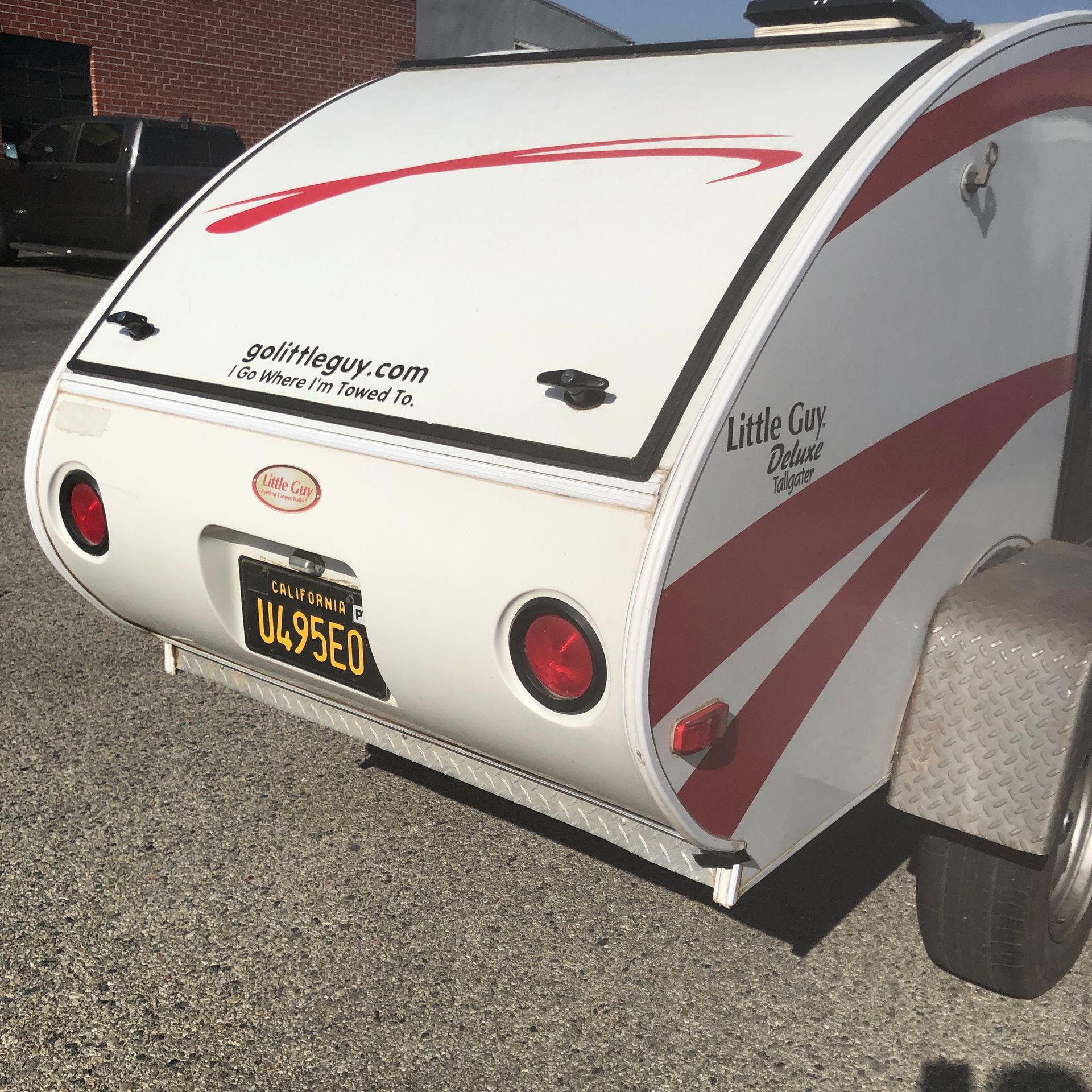 A white Little Guy teardrop camper trailer with red accents and a California license plate parked on asphalt.