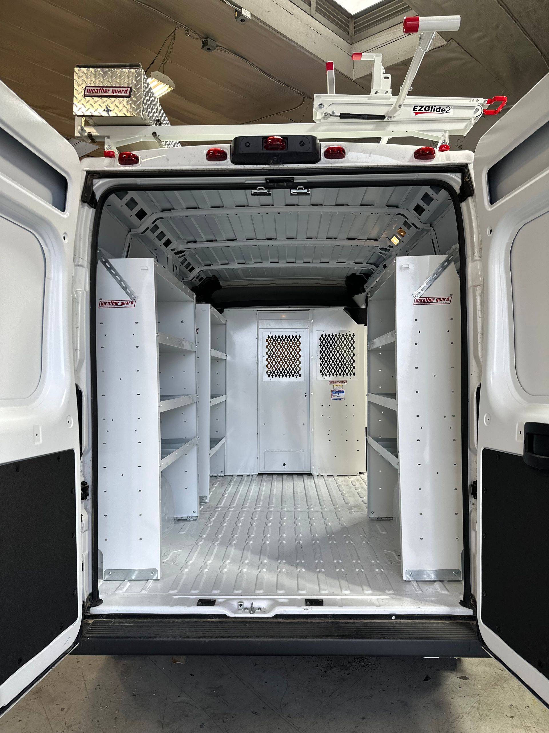 Rear view of a white van cargo area featuring white metal shelving units on both sides and a steel partition.