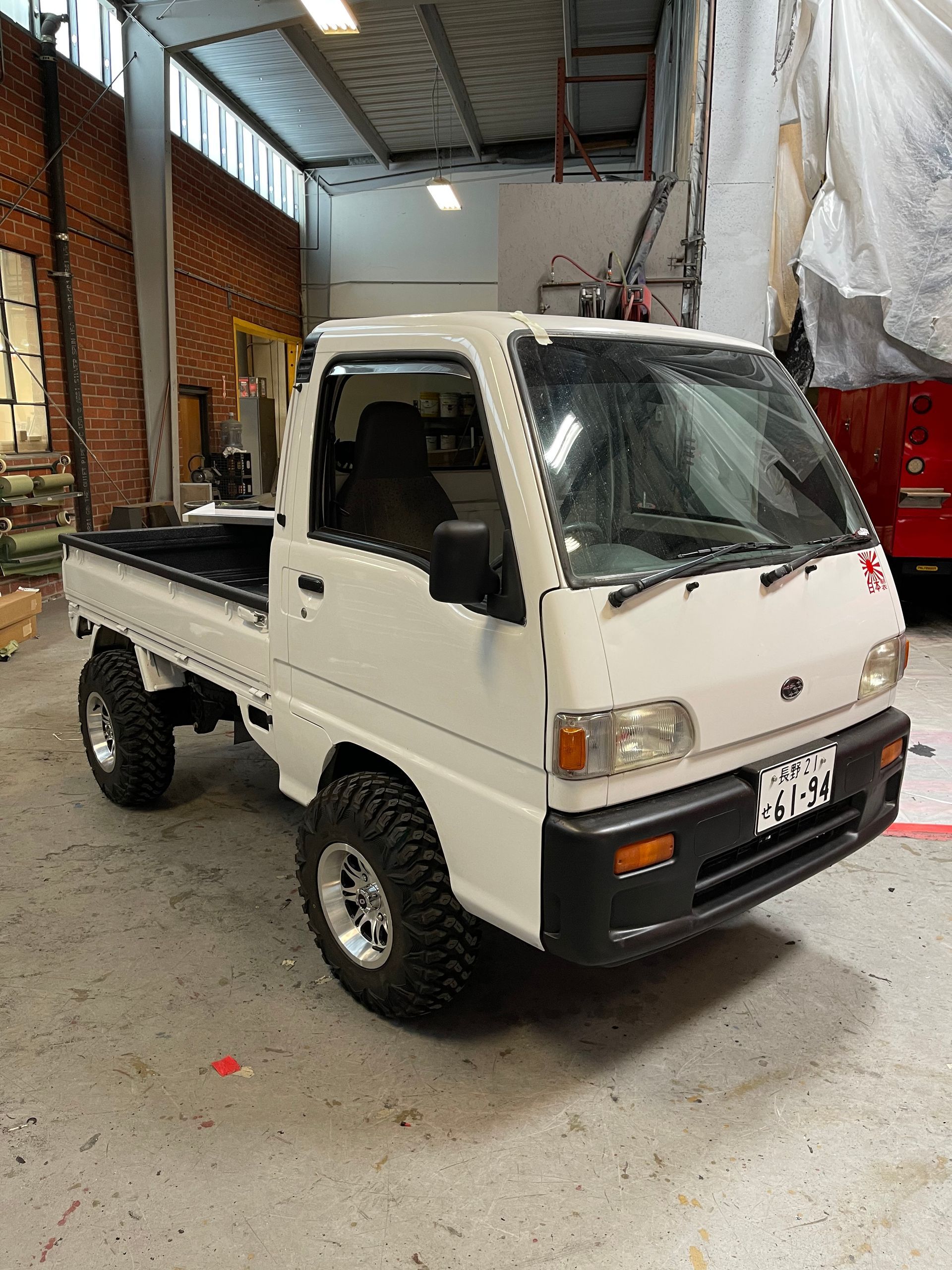 A white Kei truck with off-road tires parked inside a garage.