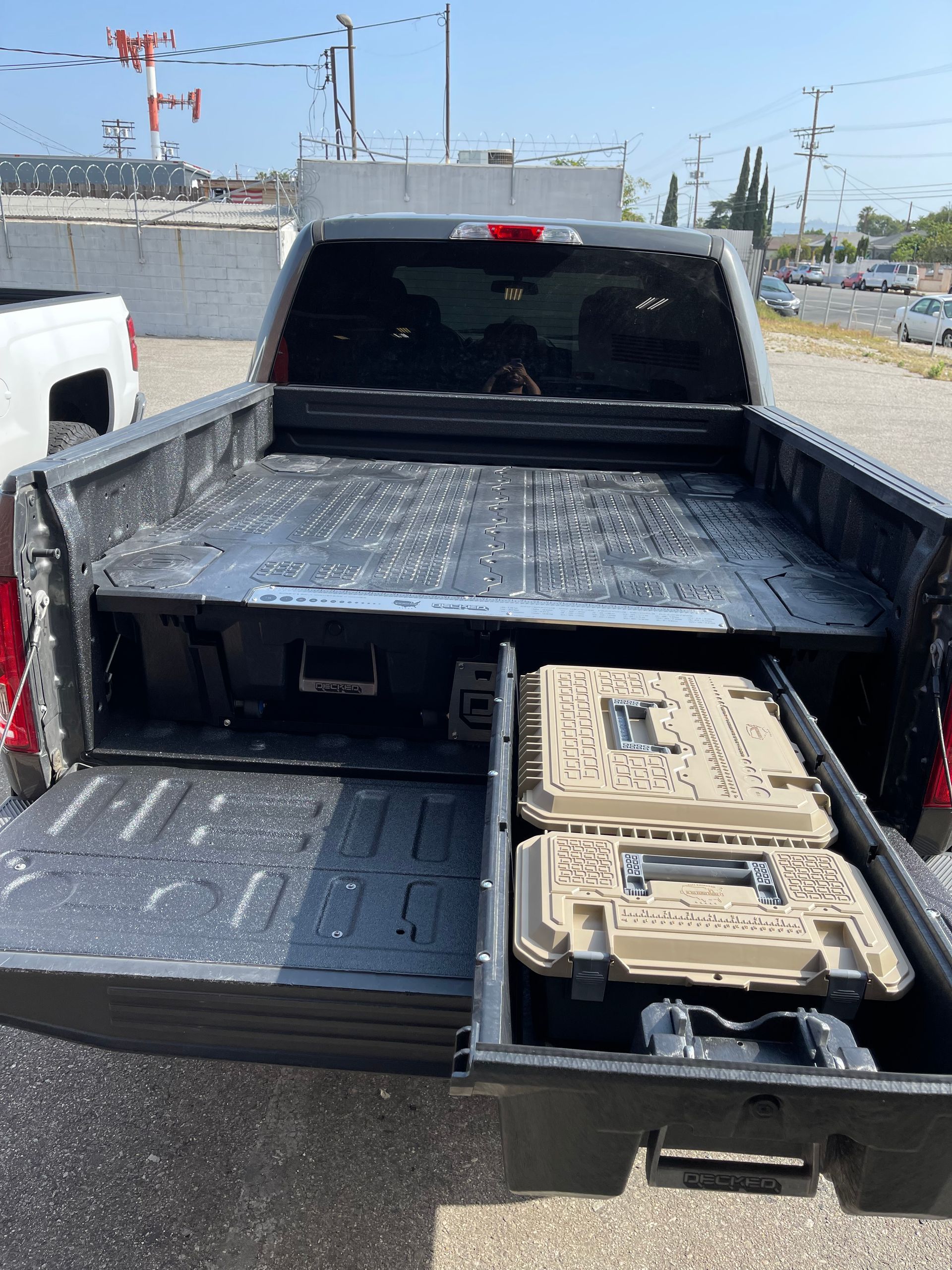 A gray pickup truck bed equipped with a sliding storage drawer system containing two tan cases, viewed from the rear.