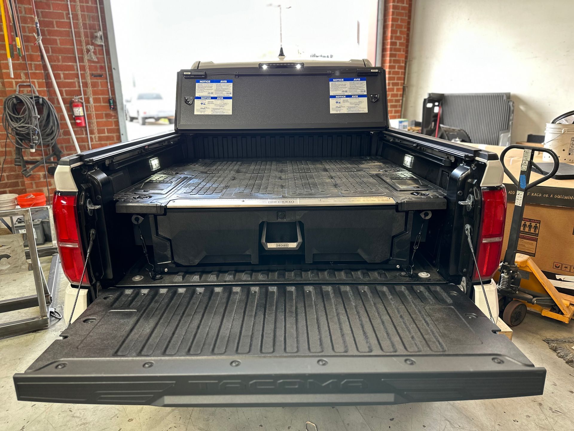 A black storage drawer system installed in the truck bed of a Toyota Tacoma with the tailgate down inside a garage.