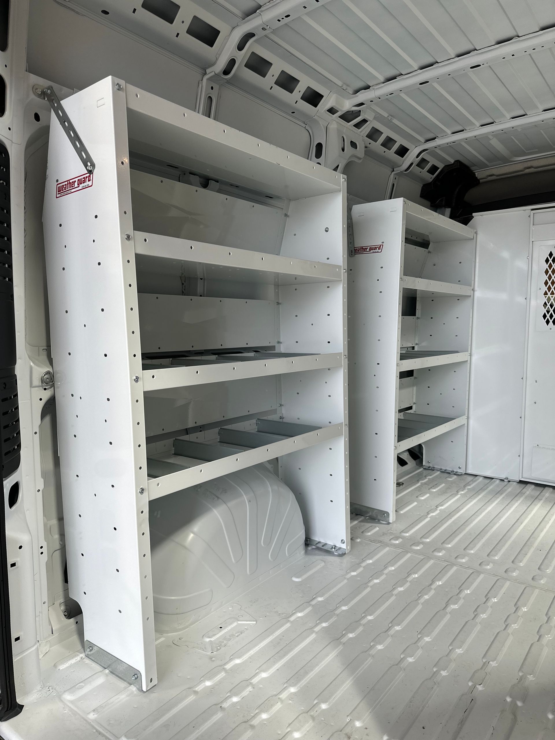 Interior of a van cargo area featuring white metal storage shelving units mounted along the walls.