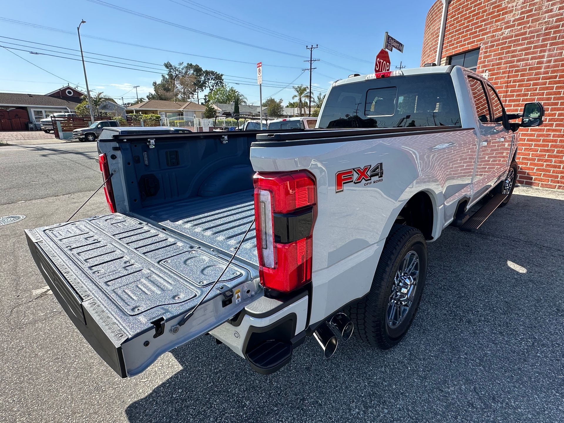 A white Ford F-250 pickup truck with its tailgate down, parked on a paved lot beside a red brick wall.