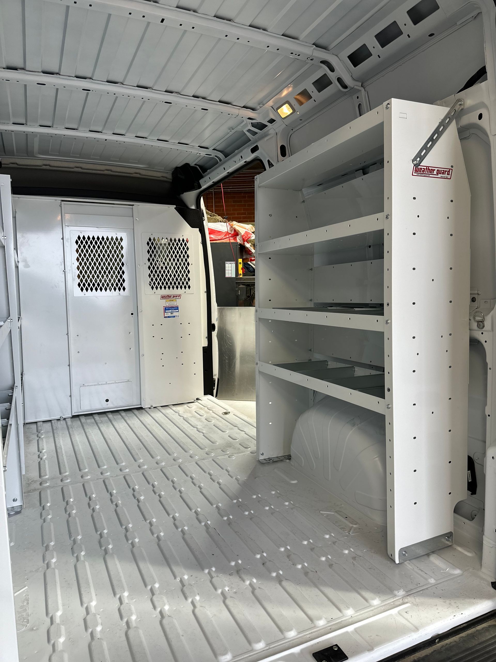 Interior of a white cargo van with industrial metal shelving on the side and a partition wall separating the cargo area.