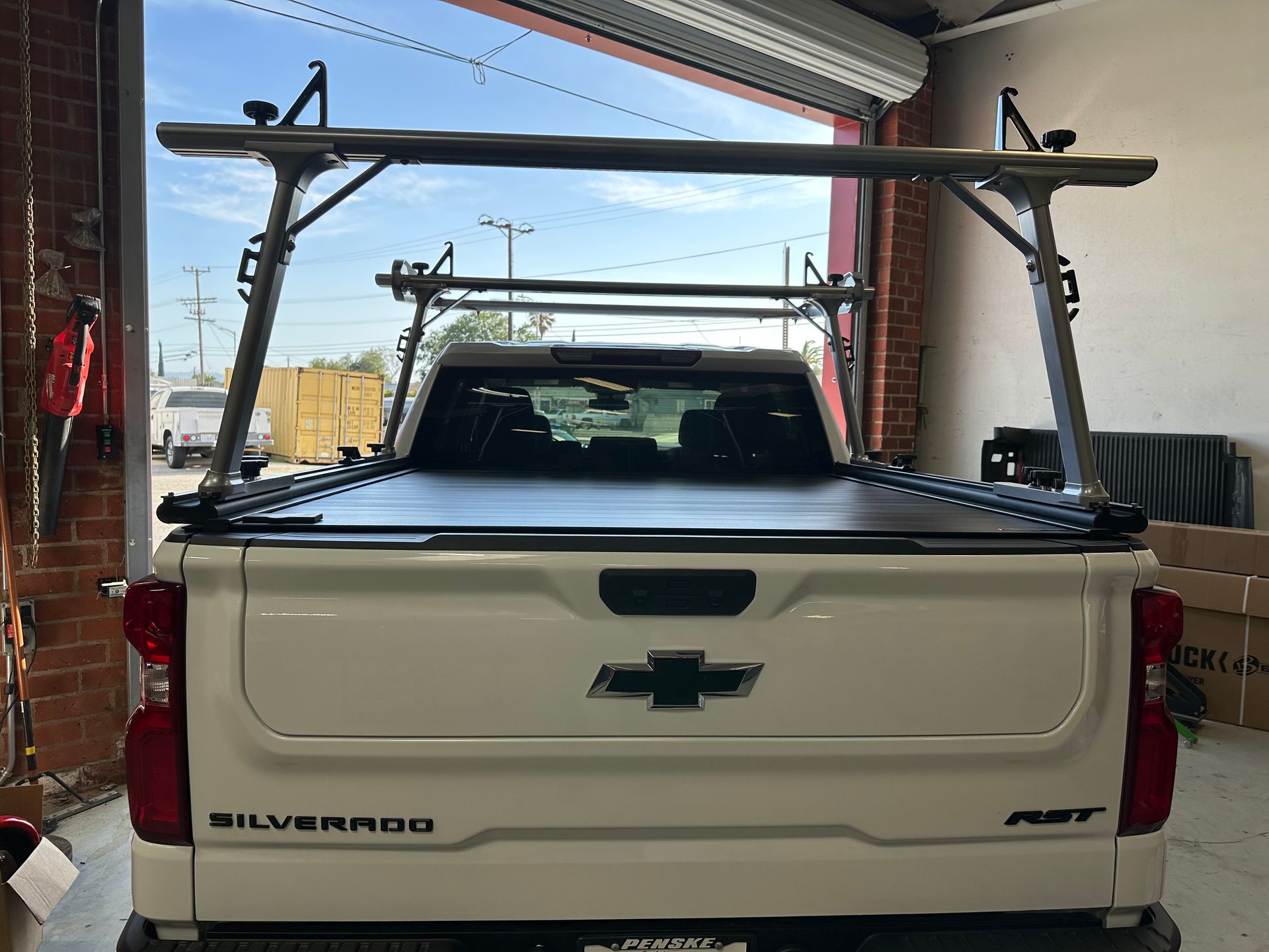 A white Chevrolet Silverado pickup truck with a black tonneau cover and a metallic ladder rack, parked inside a garage.