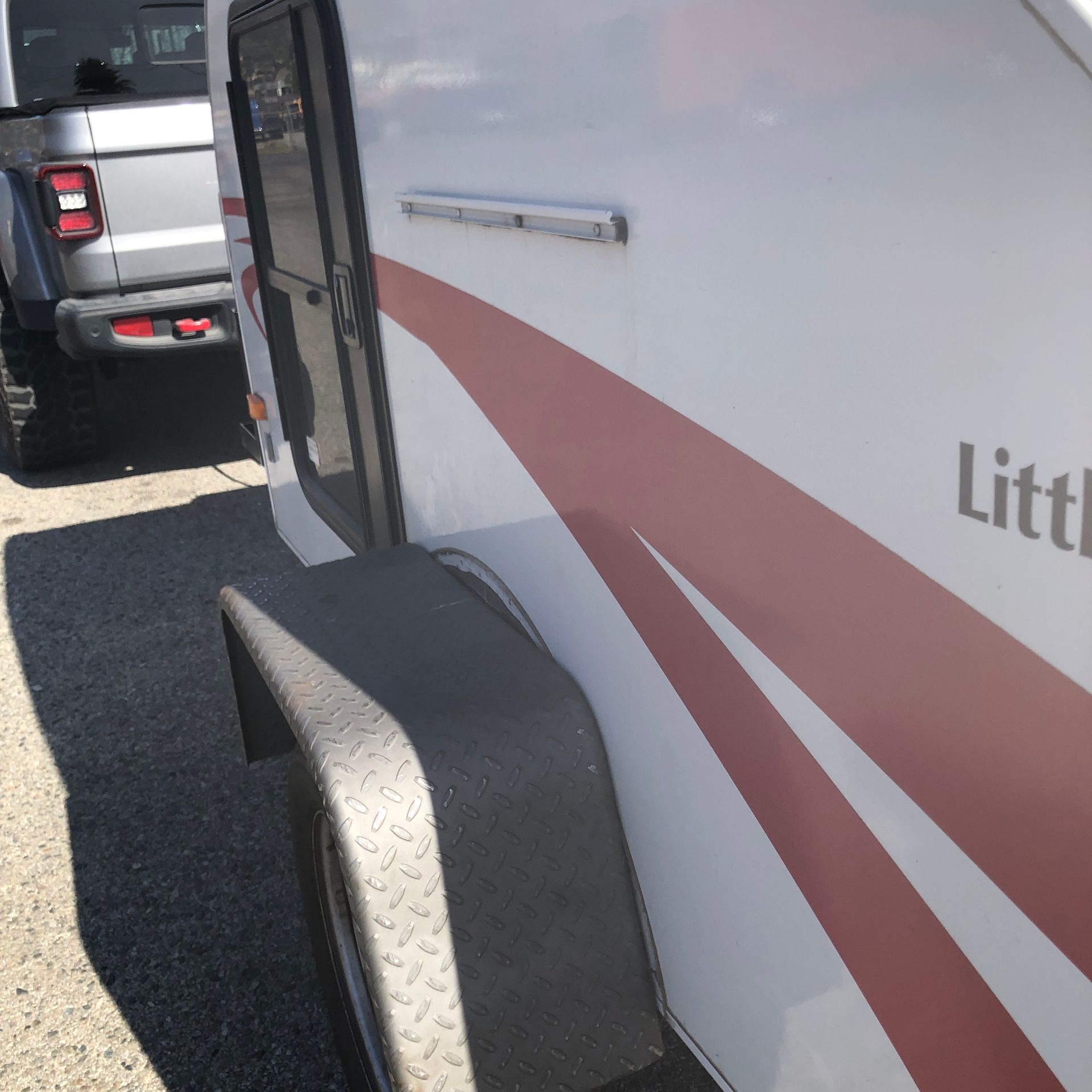 A silver SUV parked next to a white camper trailer with red accents and a textured black wheel fender.