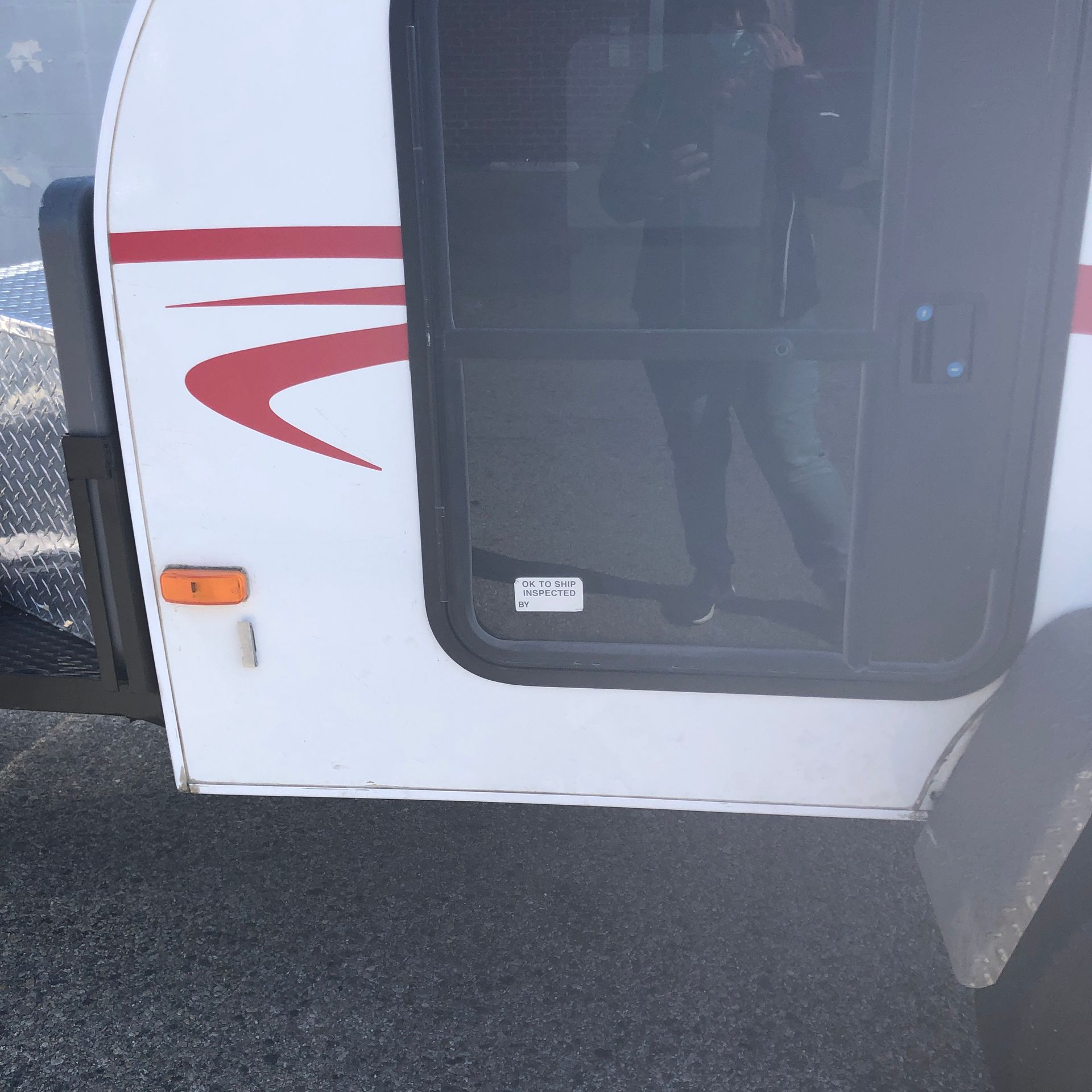 A side view of a white travel trailer featuring red graphics, a black door with a window, and a small orange marker light.