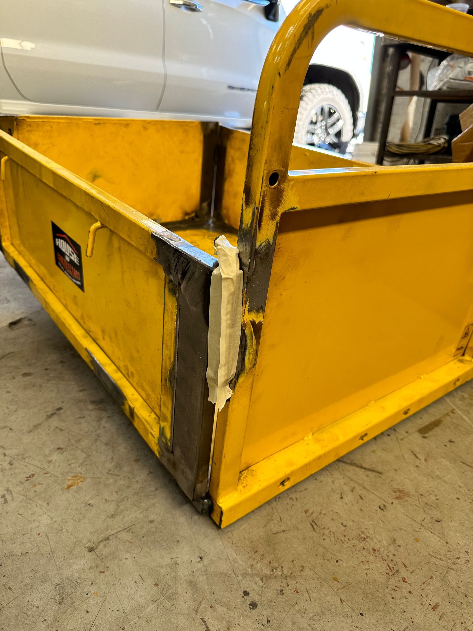 A close-up view of a yellow metal trailer corner, showing recent weld repairs and light-colored filler applied to the seam.
