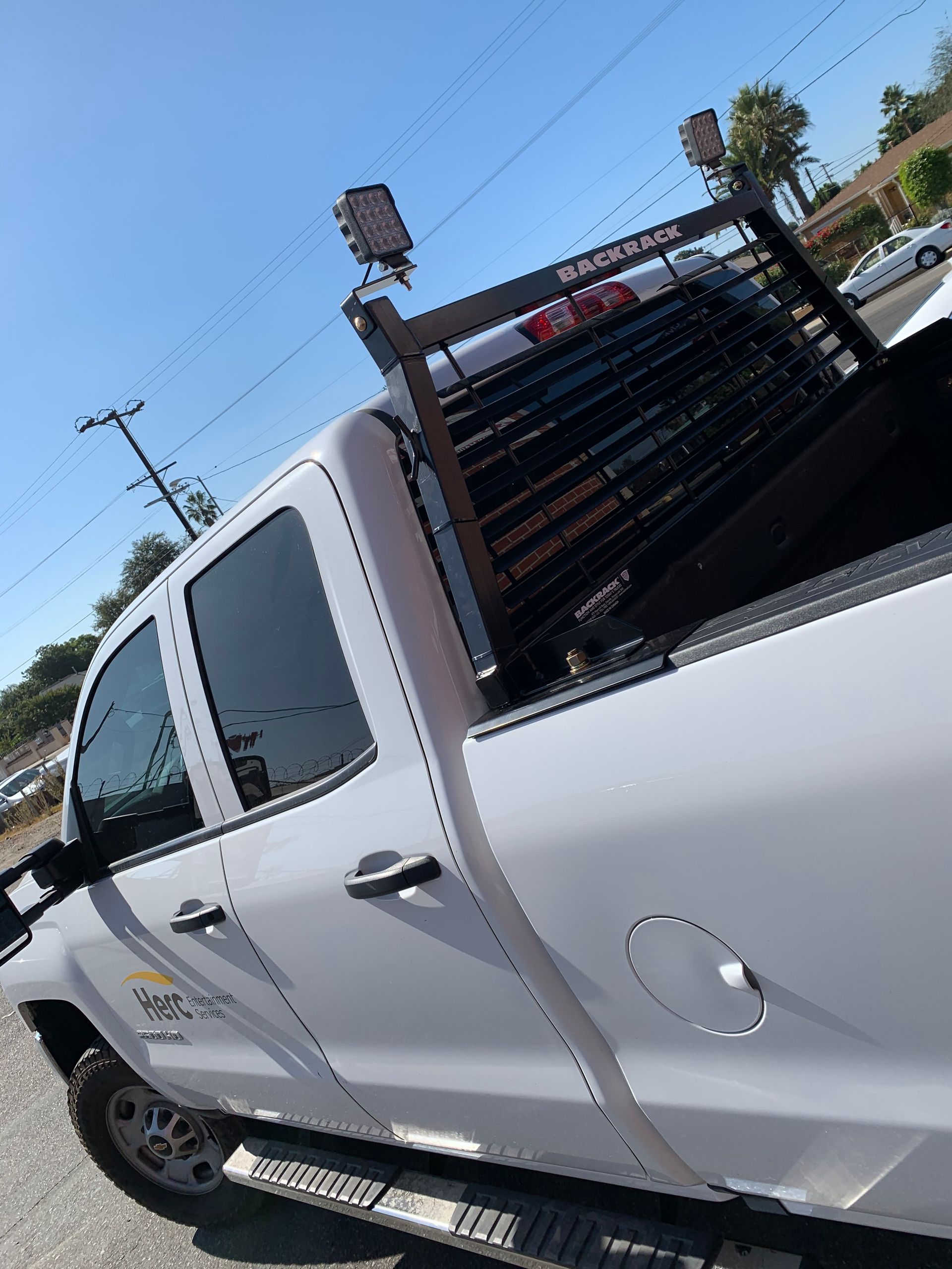 A white pickup truck with a black headache rack and utility lights, parked outdoors under a clear blue sky.