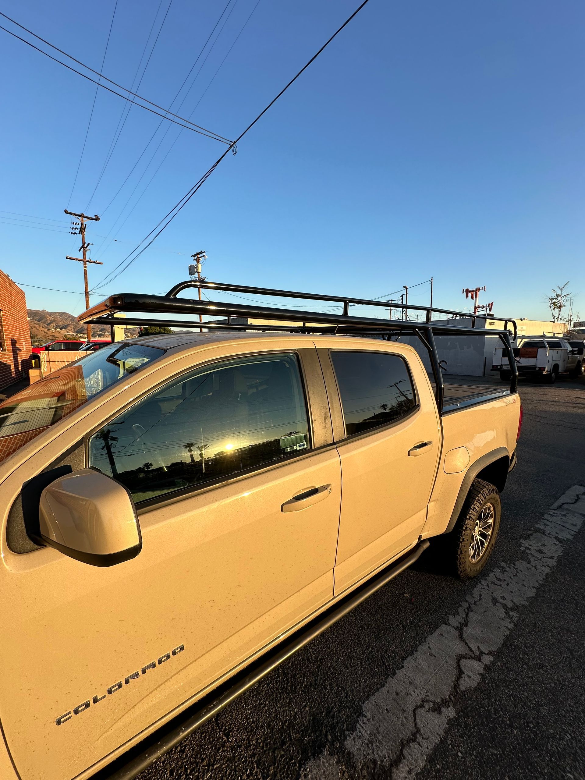 A tan Chevrolet Colorado pickup truck parked outdoors, featuring a large black cargo rack mounted above the cab and bed.