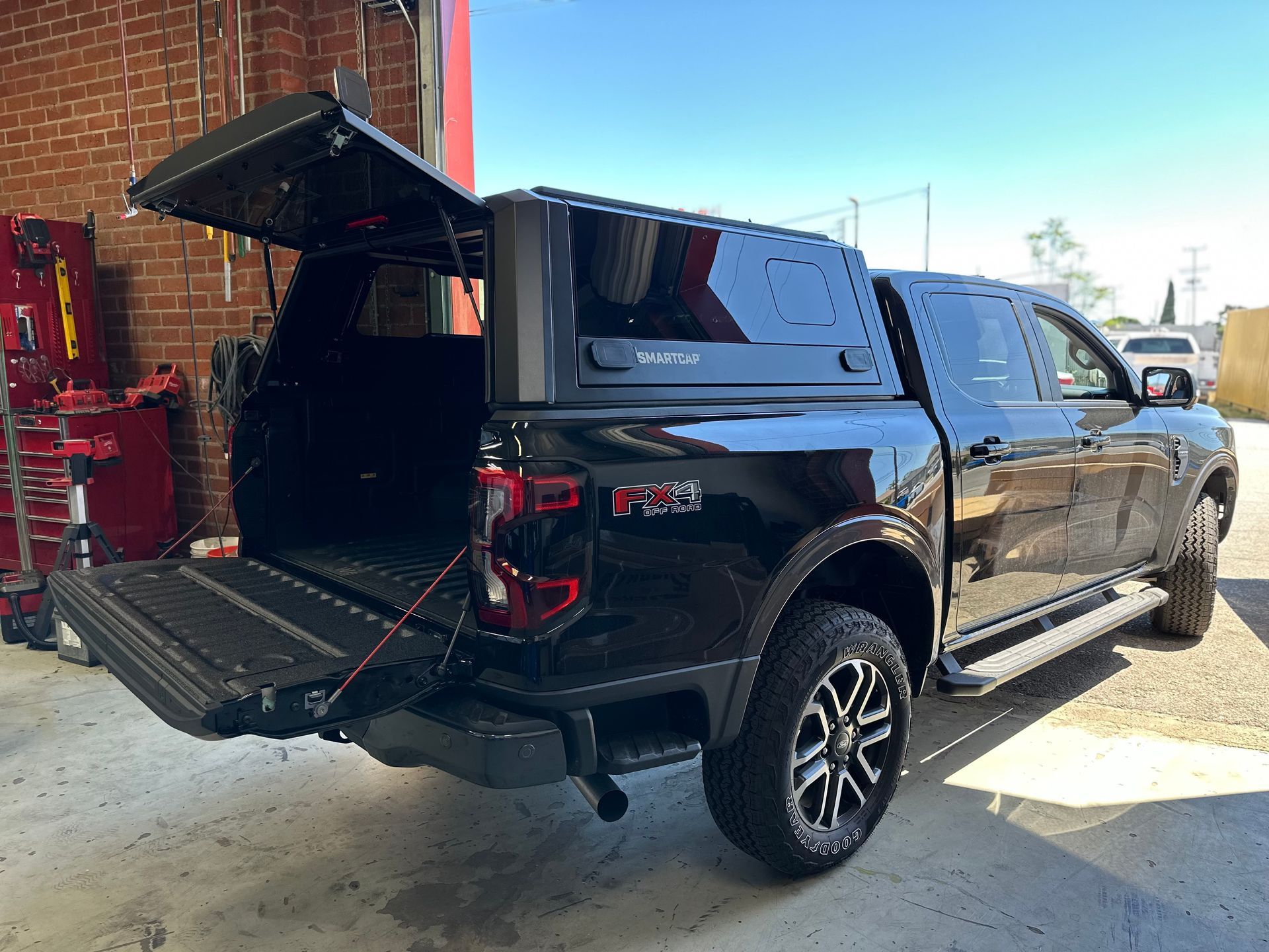 A black pickup truck with an open tailgate and a raised matching canopy parked inside a garage.