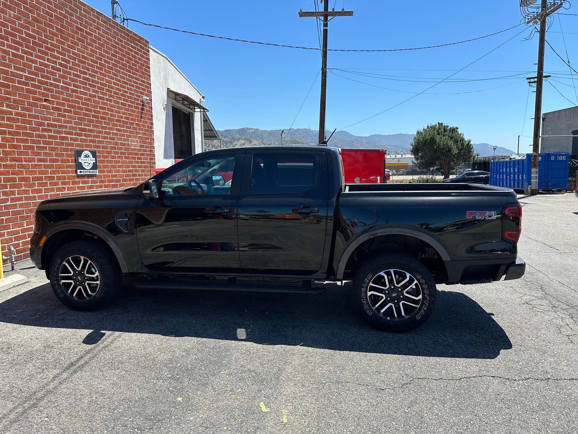 A black four-door Ford Ranger pickup truck parked on an asphalt lot beside a brick building under a clear blue sky.