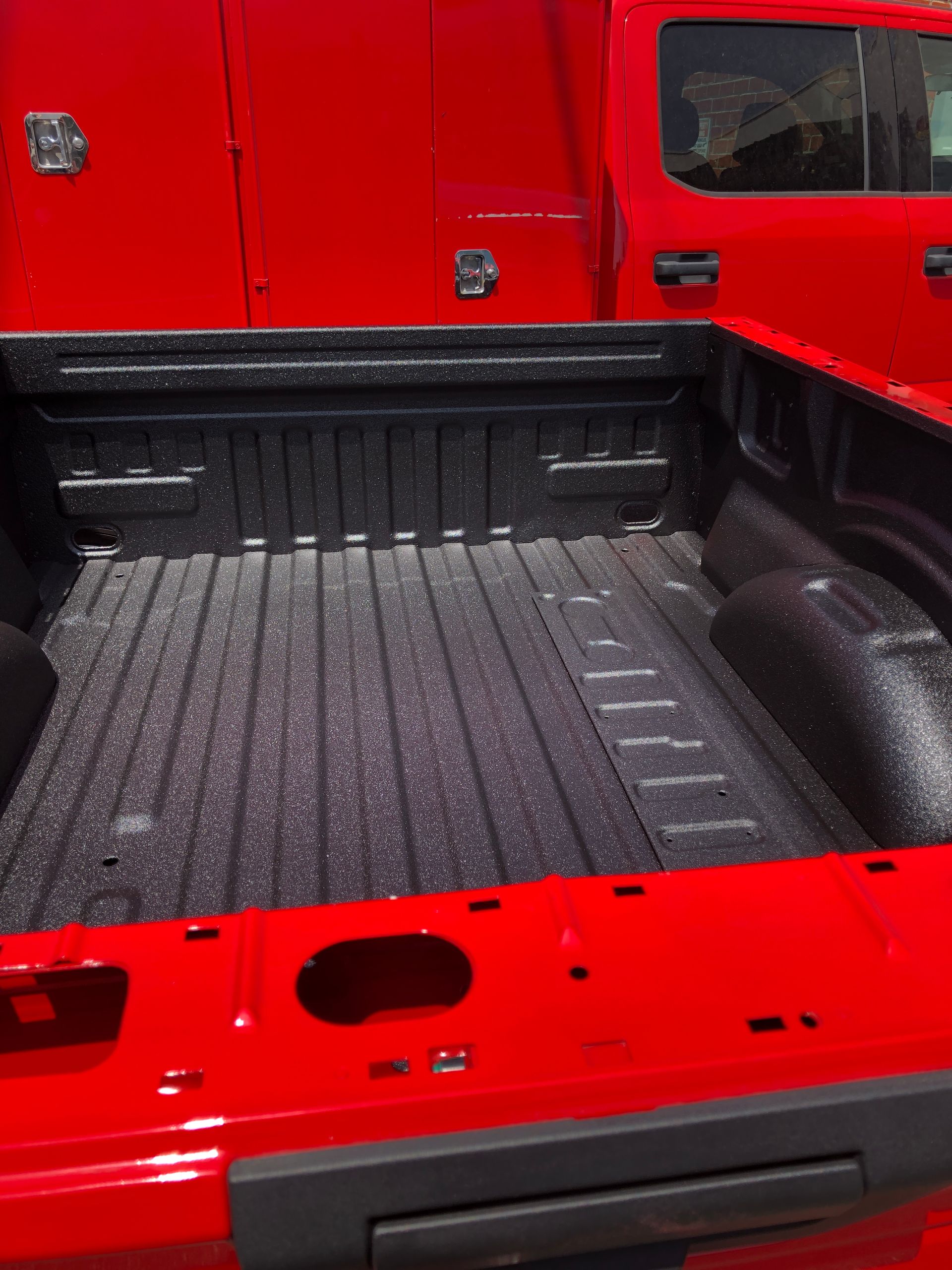 The empty cargo bed of a bright red pickup truck, featuring a black textured spray-in bed liner.