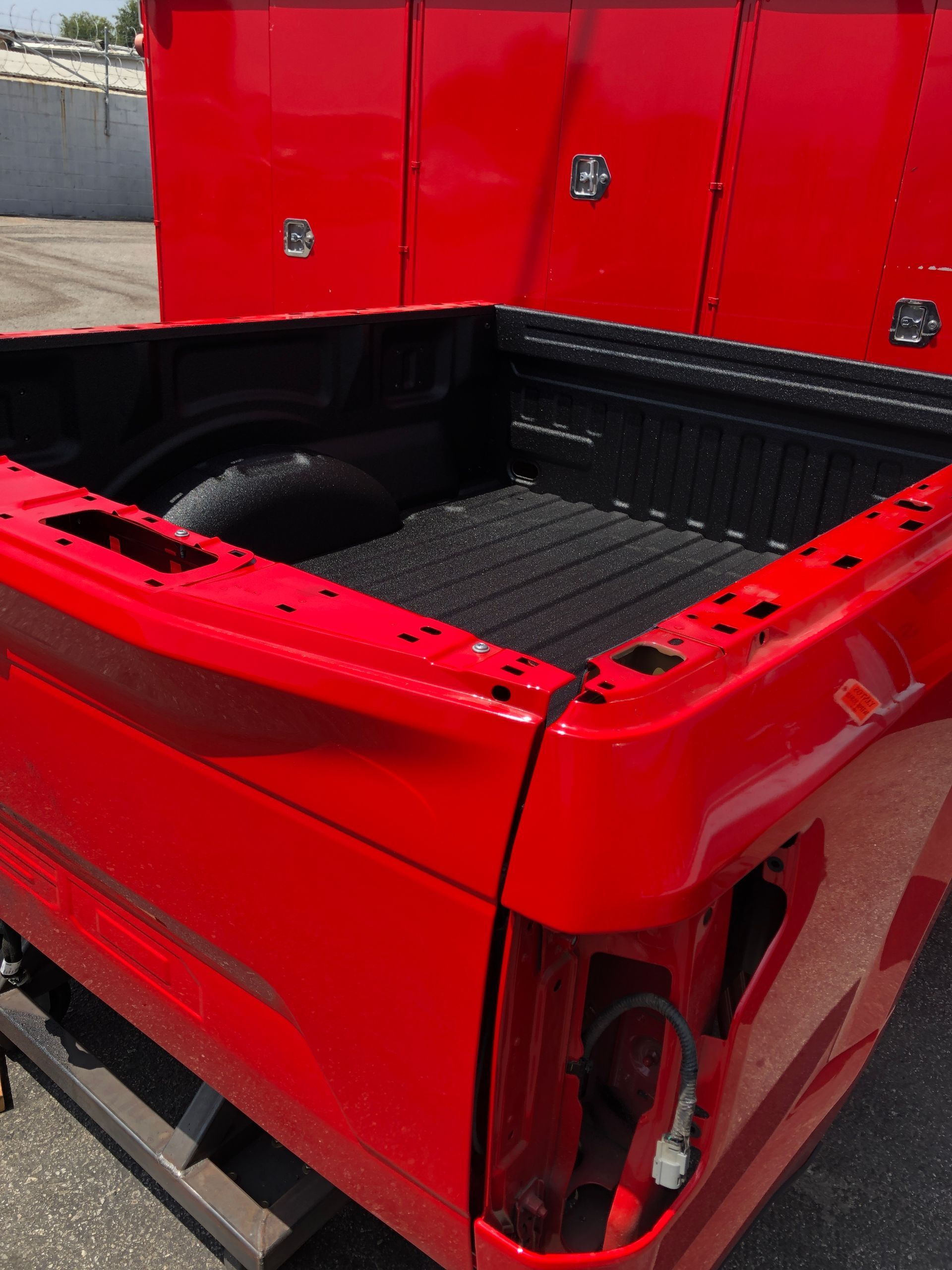 A red pickup truck bed with a black liner, missing its tailgate and taillight, sitting on a pallet outdoors.