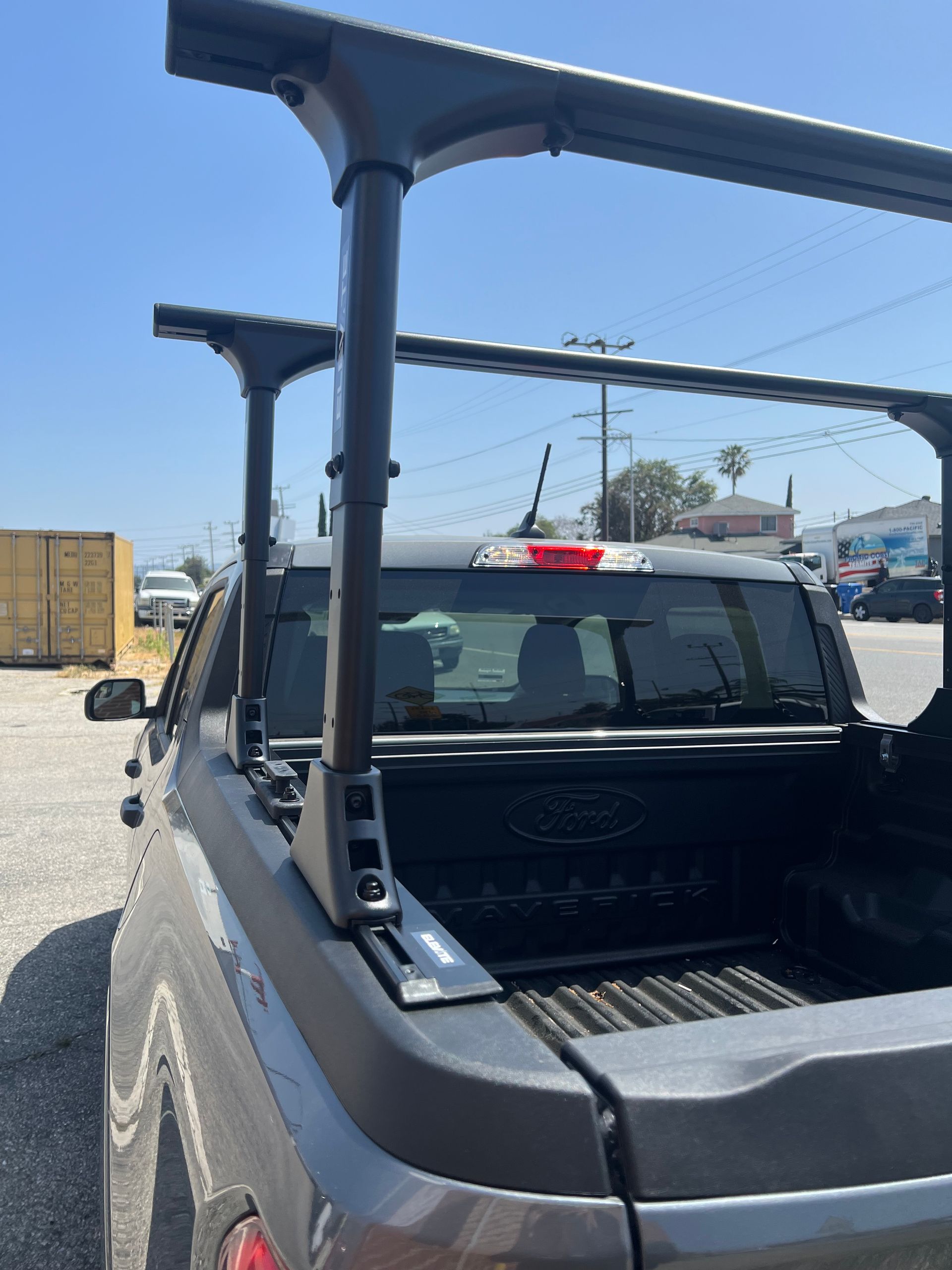 A black adjustable truck bed rack system mounted on the sides of a grey Ford pickup truck under a clear blue sky.
