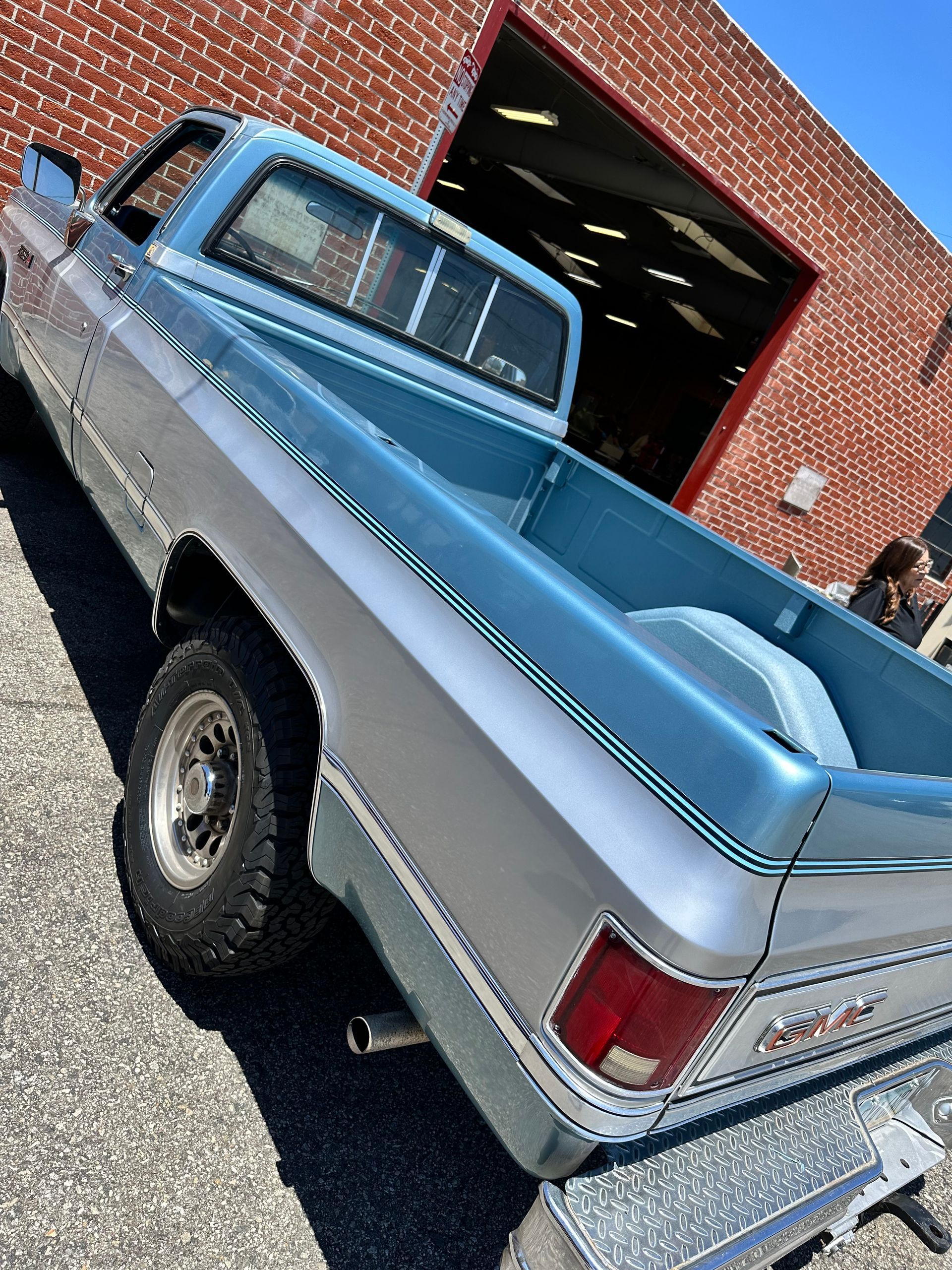 A two-tone blue and silver pickup truck parked on asphalt in front of a red brick building.