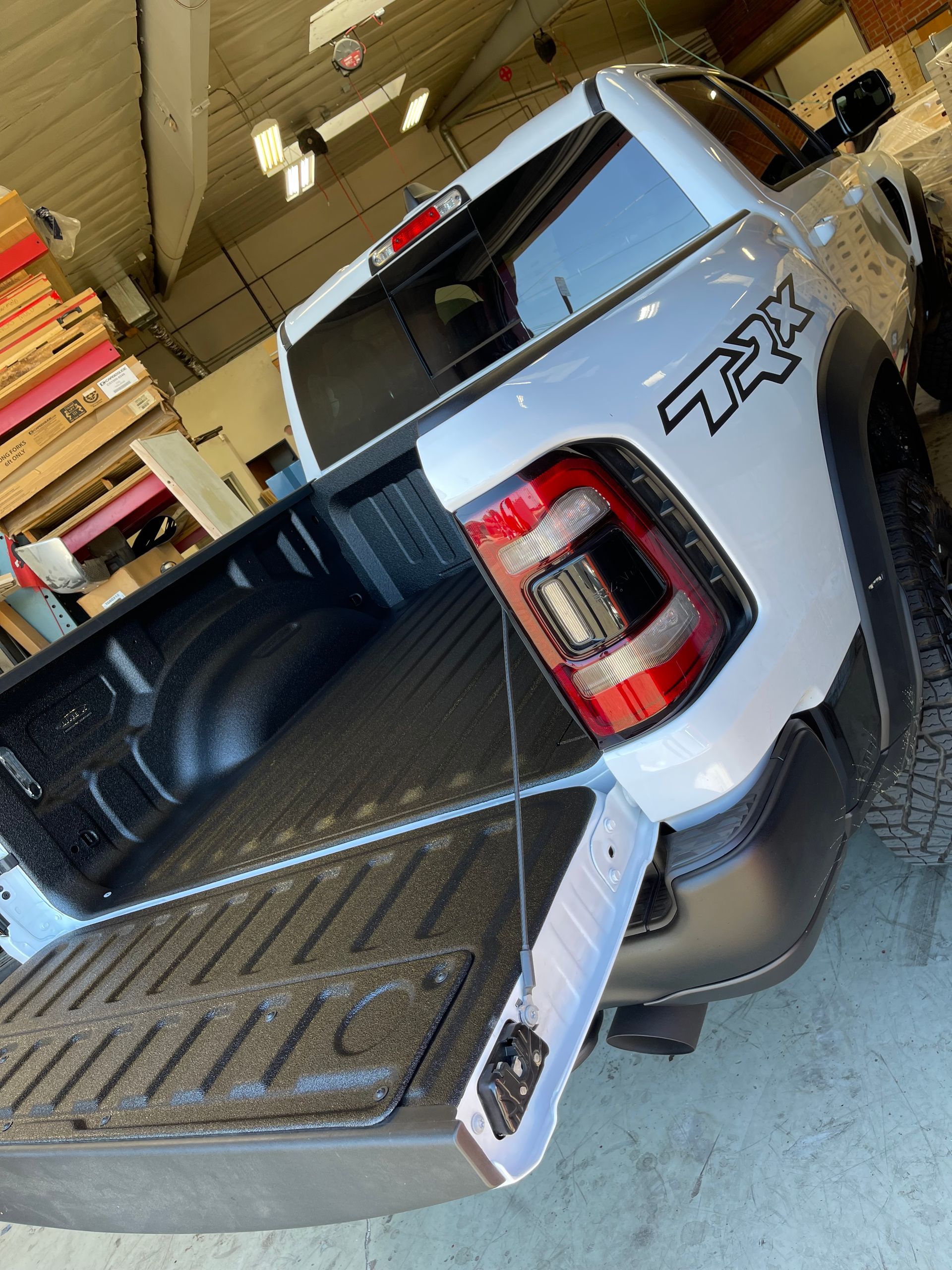 A light-colored Ram TRX pickup truck with an open tailgate, parked inside a warehouse storage area.