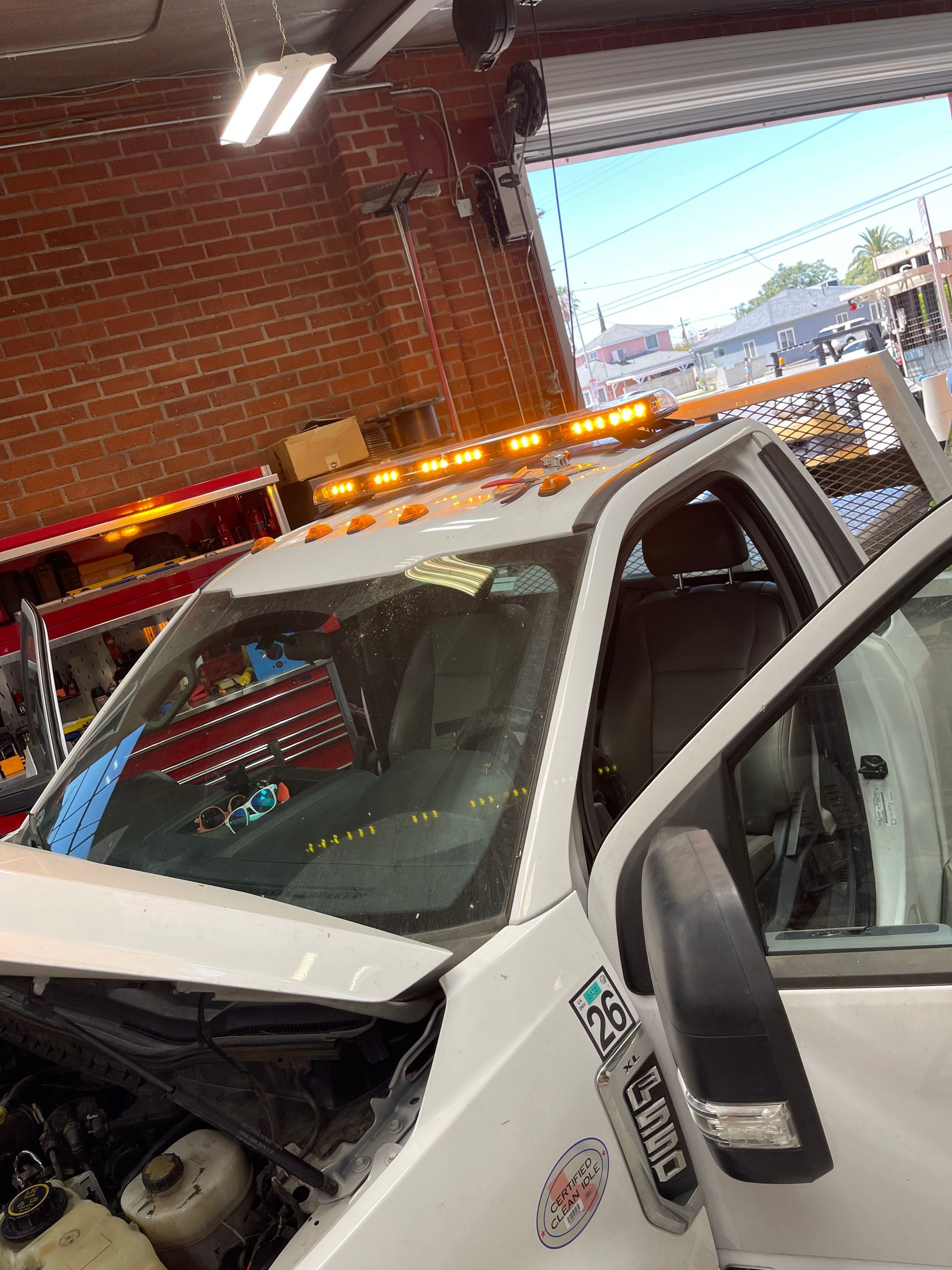 A white utility truck with emergency roof lights parked inside a workshop with a brick wall.