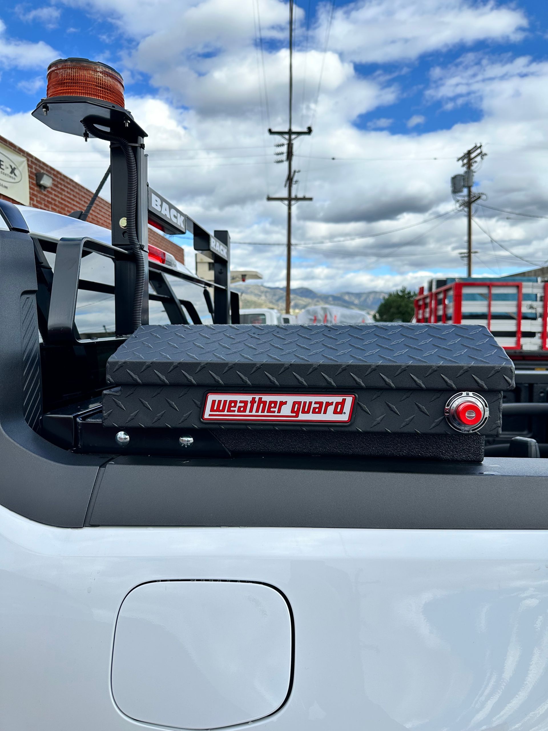 A black Weather Guard truck bed storage box mounted on the side of a white truck, next to an amber warning light.