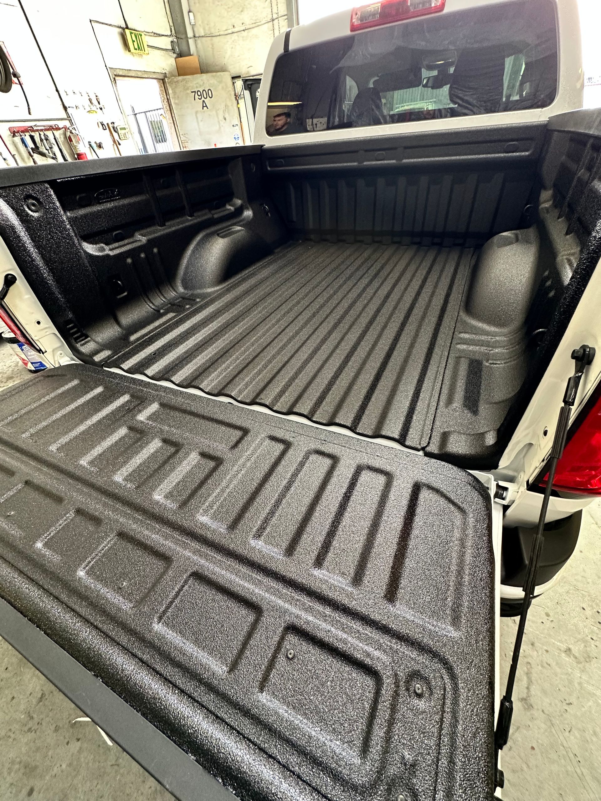 The open tailgate and empty bed of a white pickup truck, featuring a textured black protective spray-on liner.