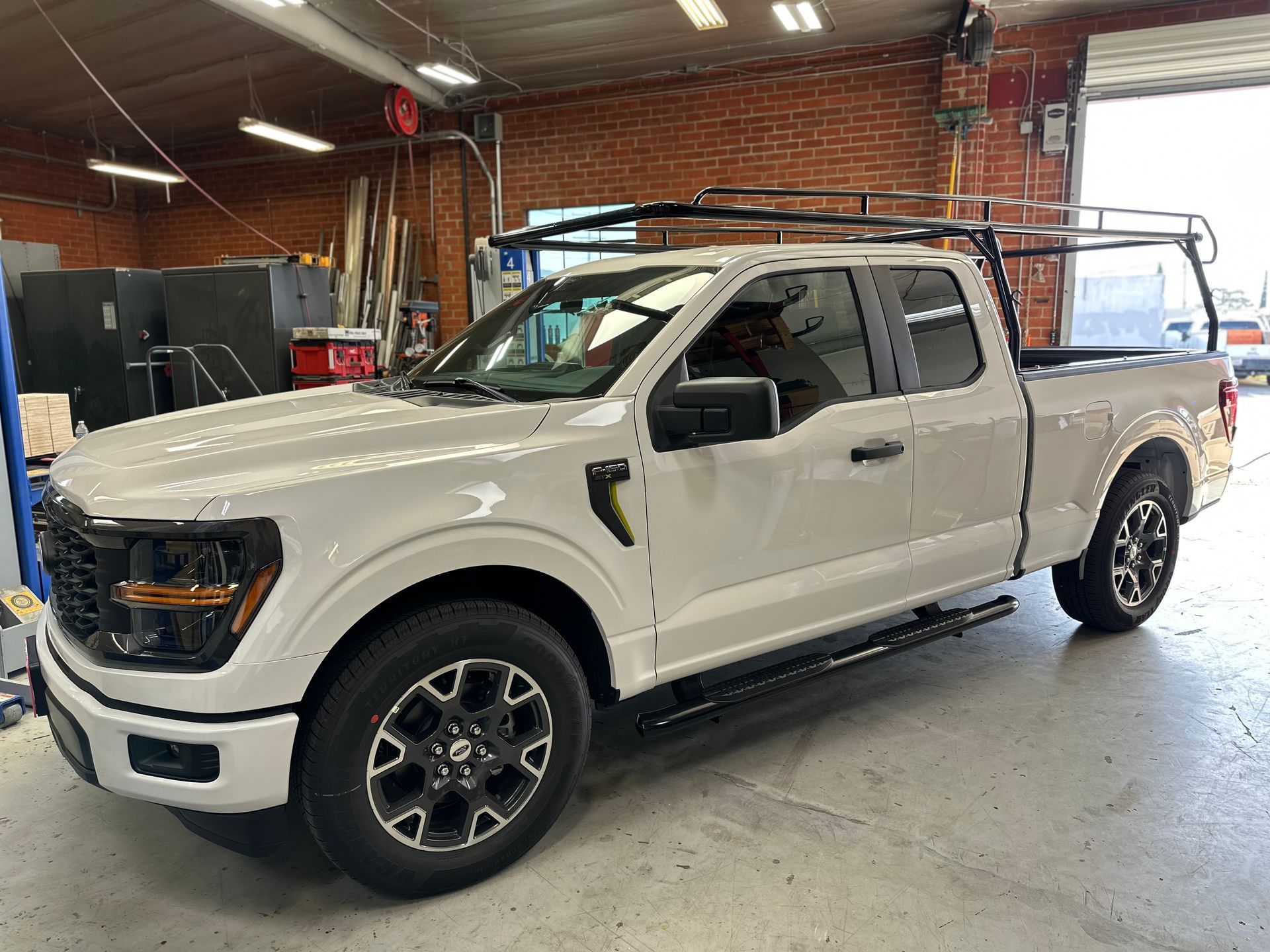 A white Ford F-150 extended cab truck with a black roof rack parked inside a warehouse with brick walls.
