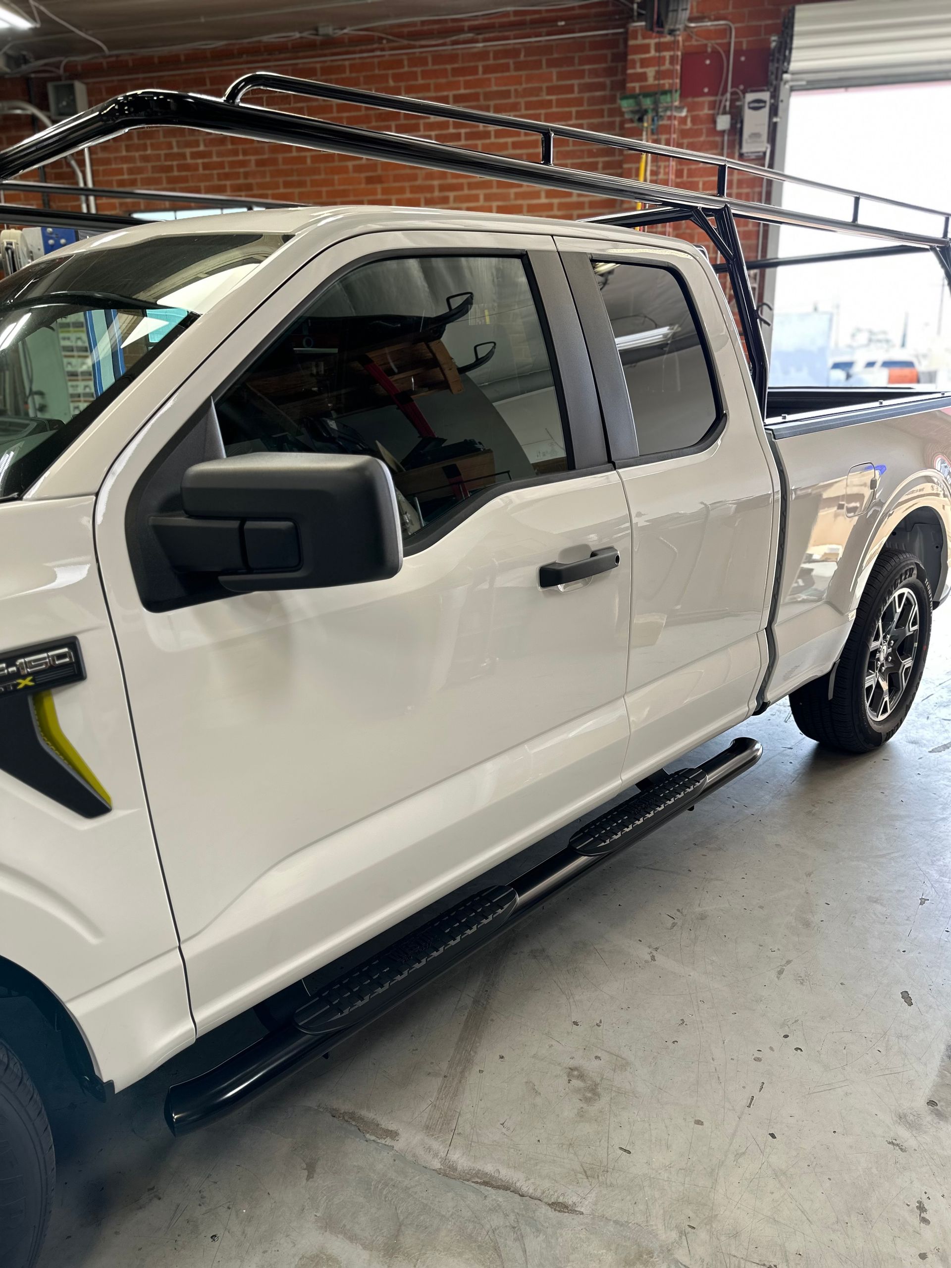 Side view of a white Ford F-150 pickup truck with a black roof rack and side steps, parked inside a garage.