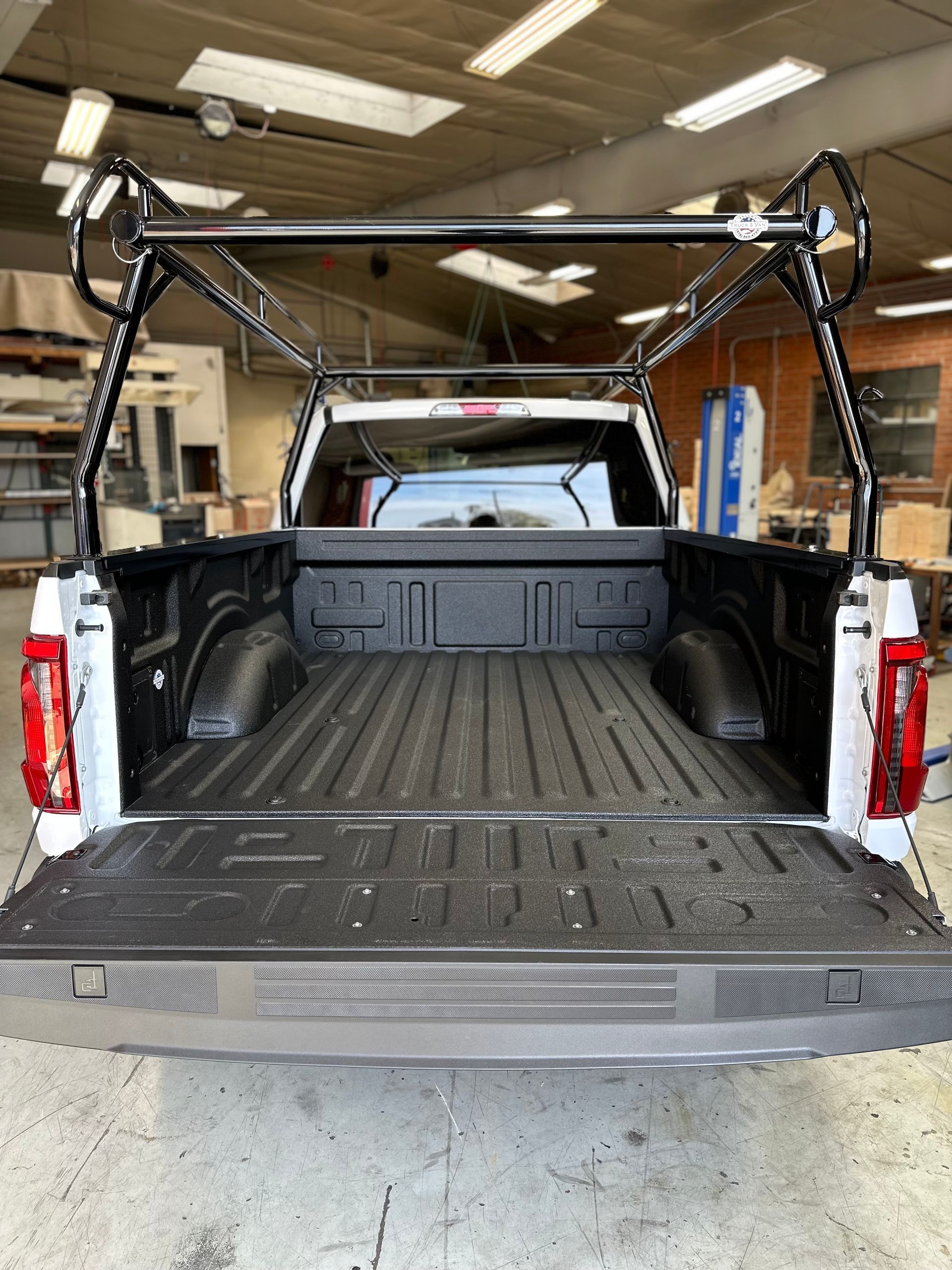 The rear view of a white pickup truck with an open tailgate and a black metal ladder rack installed over the cargo bed.