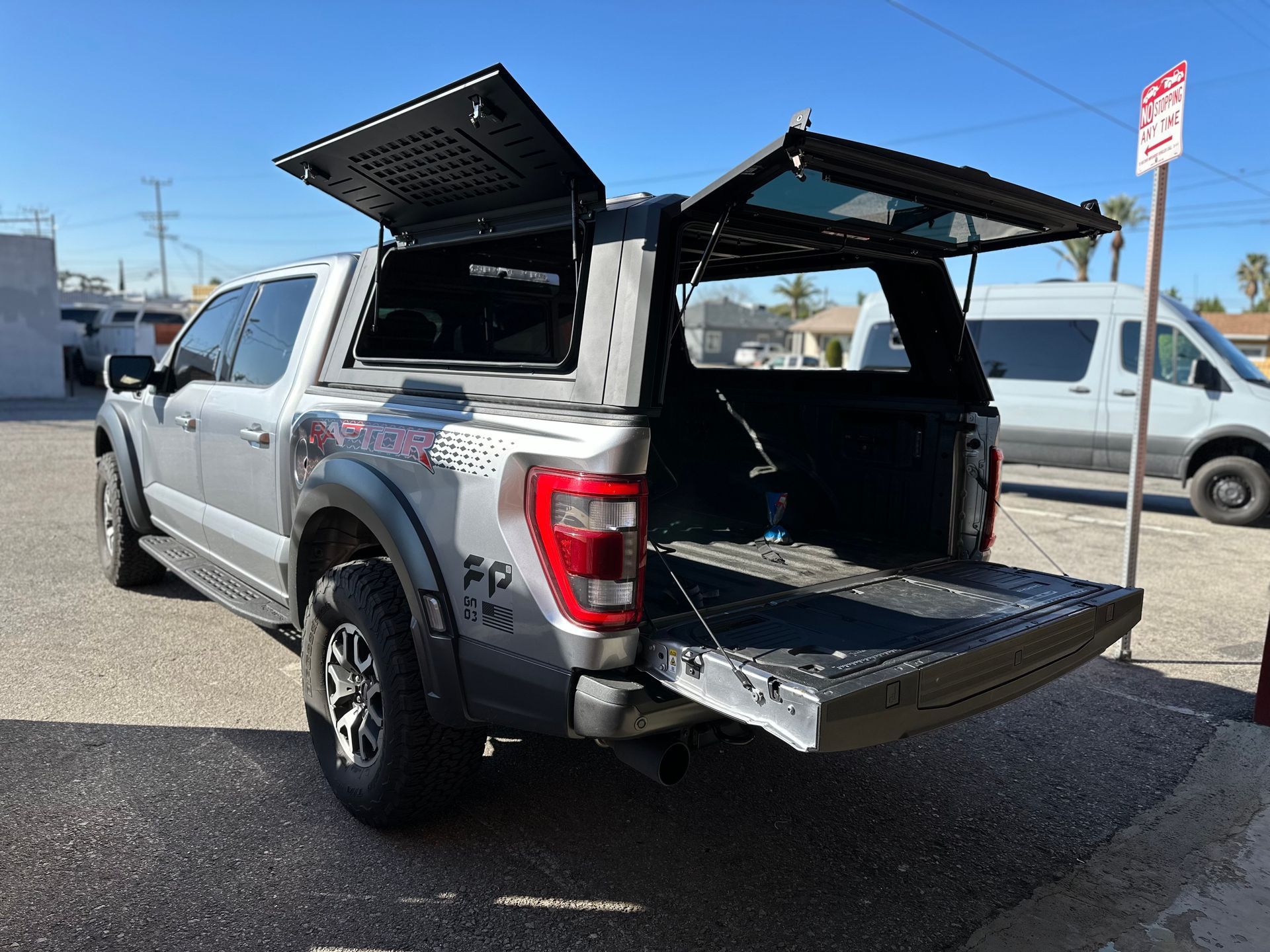 Silver pickup truck parked on asphalt with its bed cover and tailgate open, showing the cargo space.