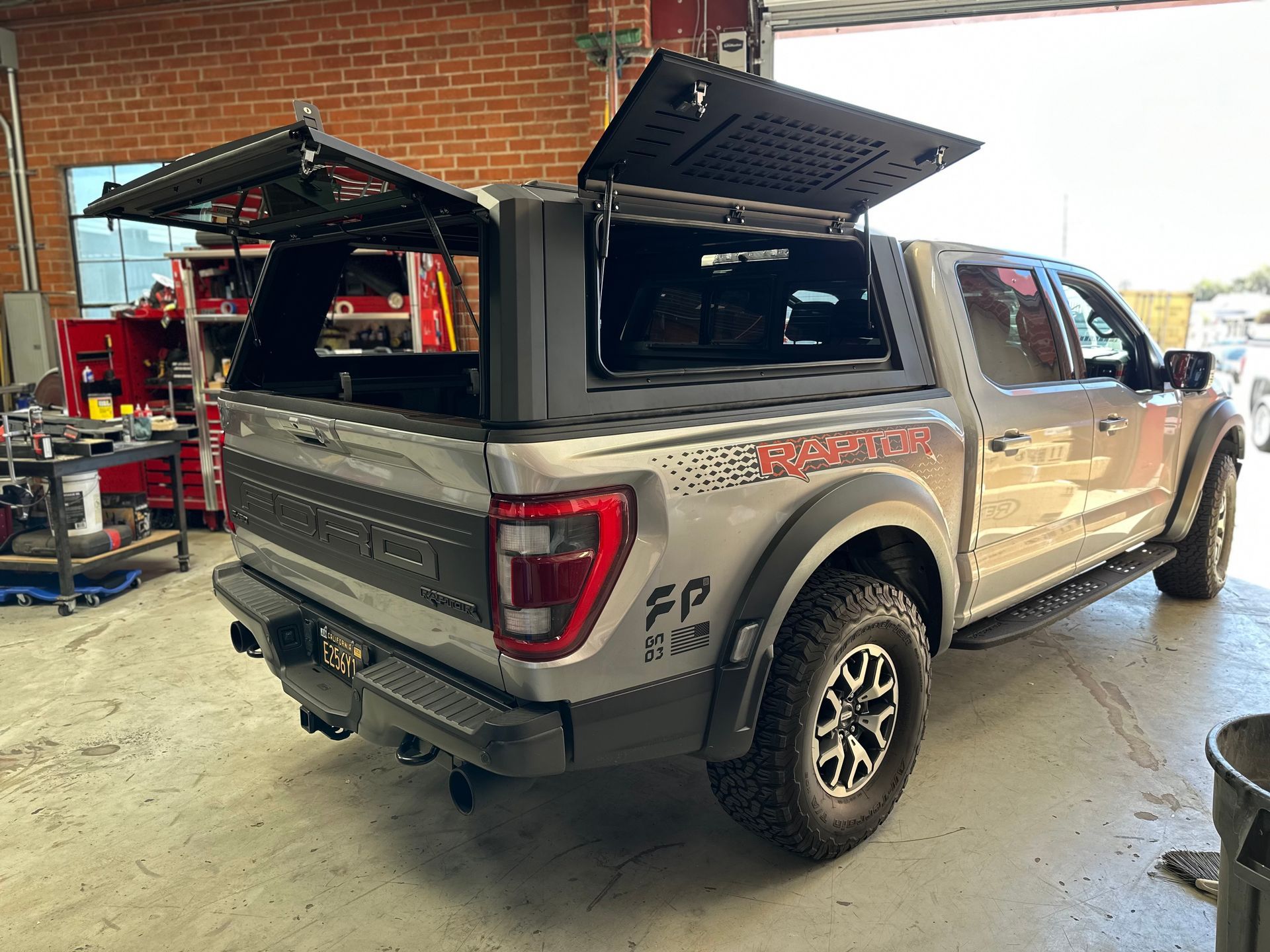 Silver Ford Raptor pickup truck inside a garage with its aftermarket truck bed canopy doors open.