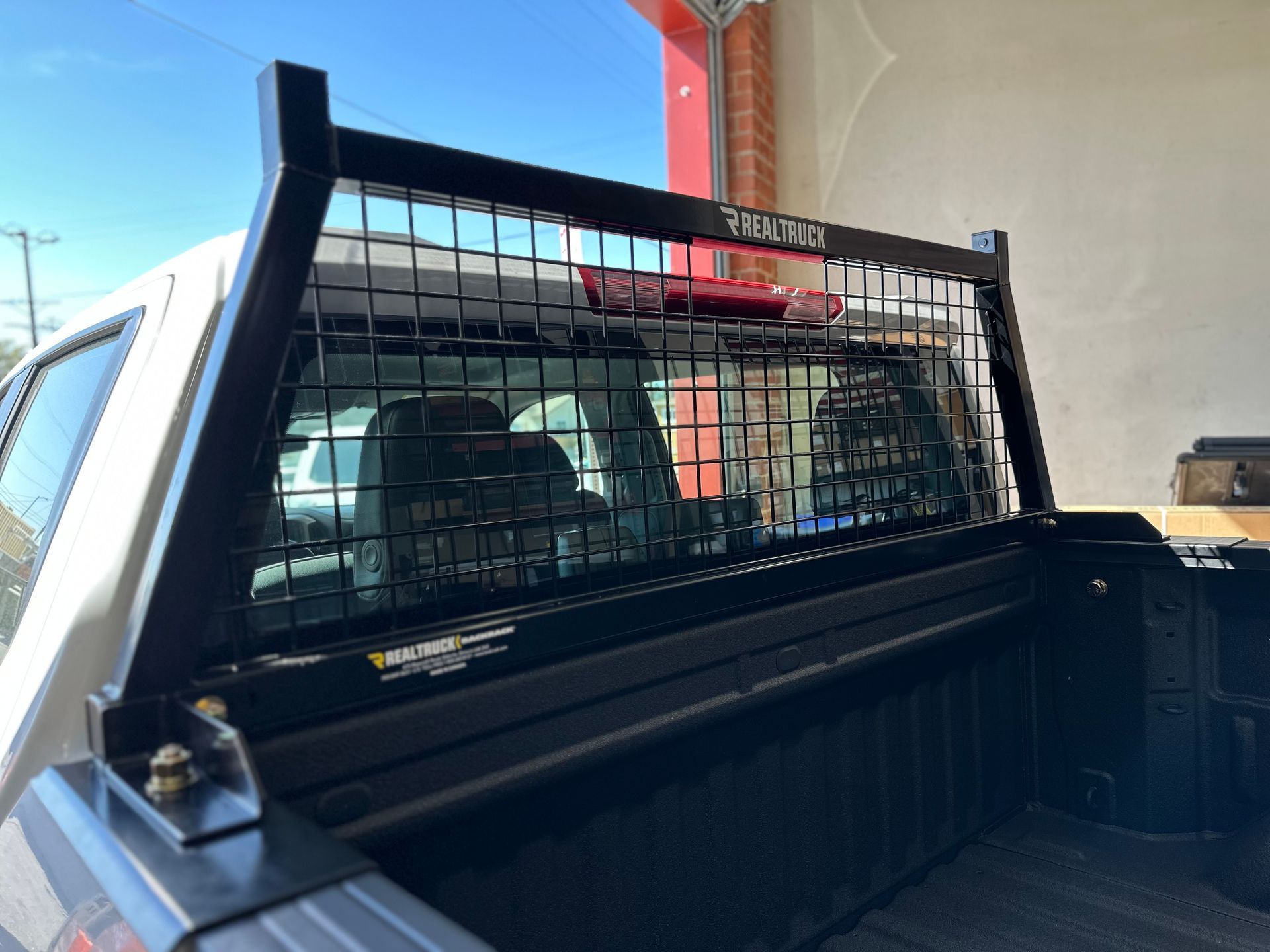 A black metal headache rack with a wire mesh grid installed on the bed of a white pickup truck.