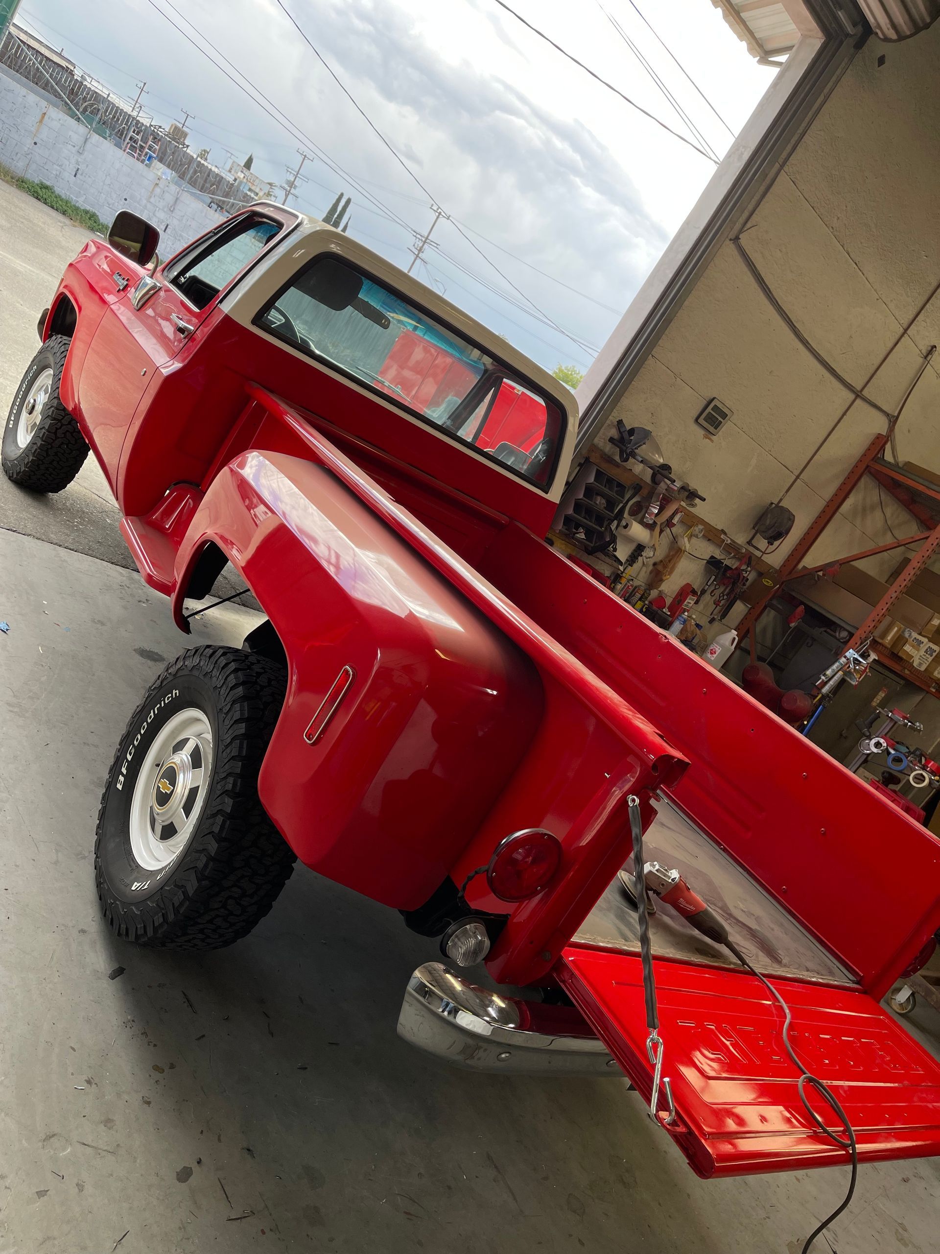 A bright red, vintage Chevrolet pickup truck with a white cab roof parked in a workshop.