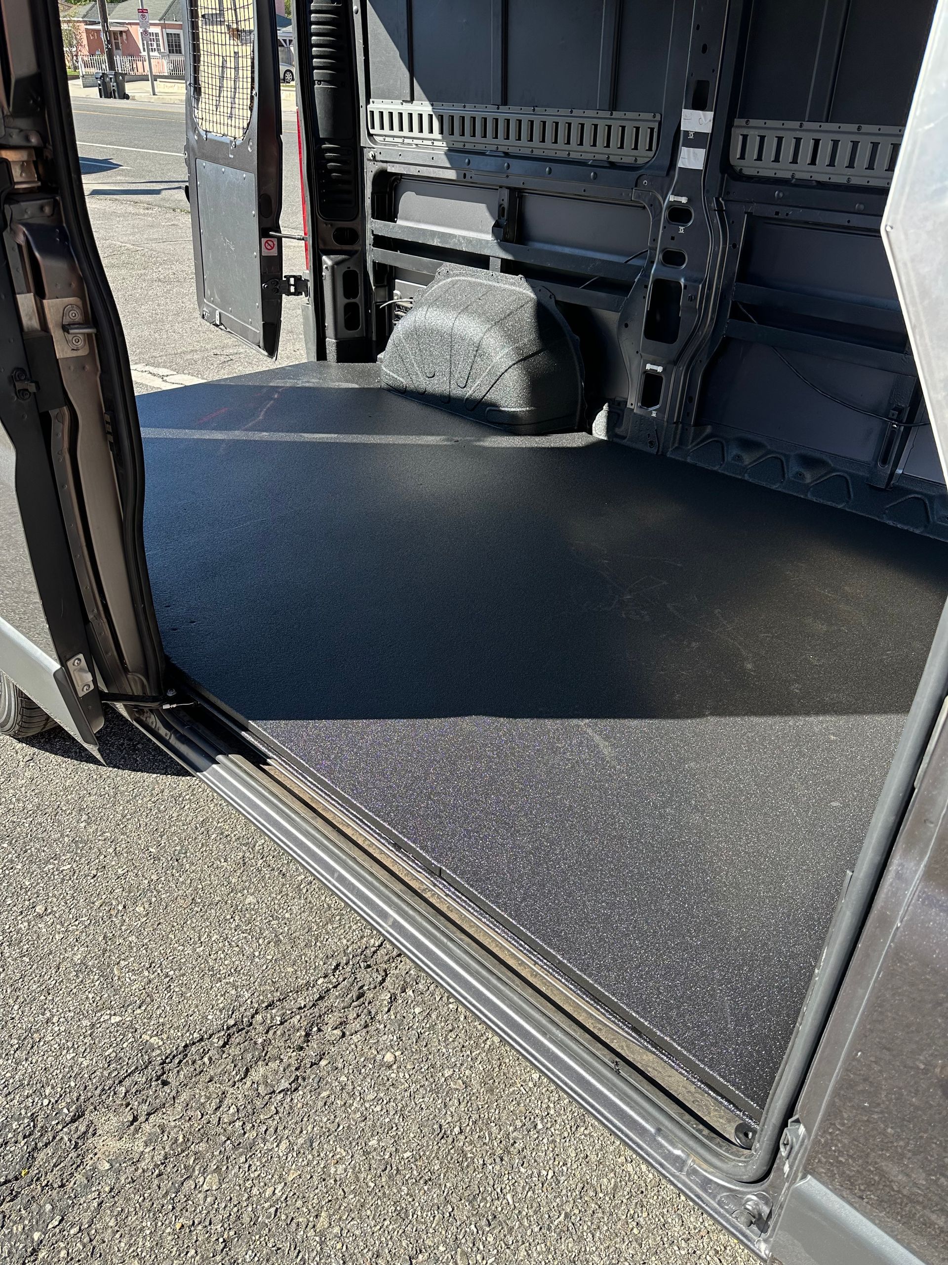 Open sliding door of a commercial van showing a dark, speckled, slip-resistant floor liner and metal cargo tracks.