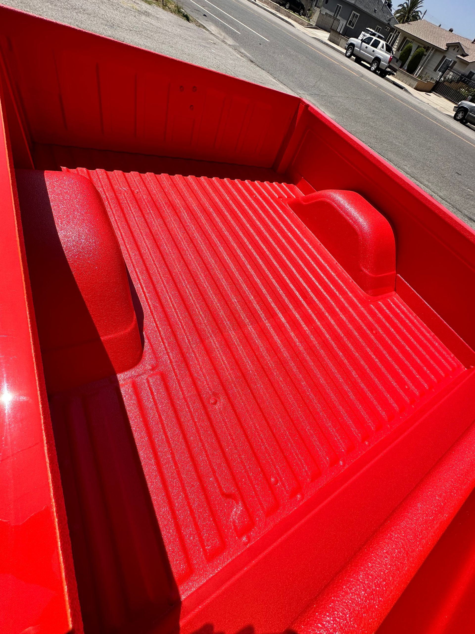 A bright red, textured truck bed liner in a pickup truck parked on a residential street.