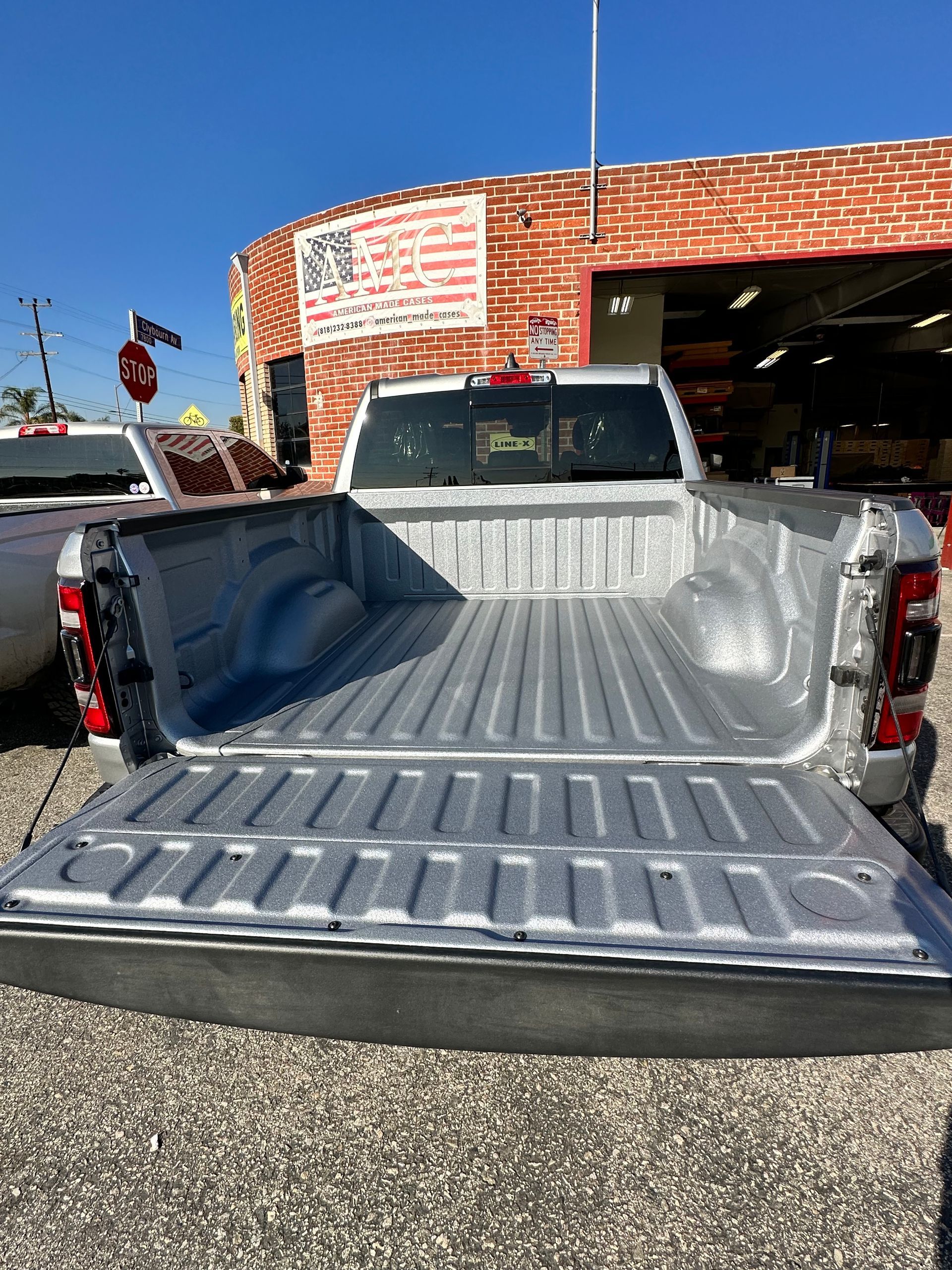 A silver truck bed with a spray-in liner, featuring a lowered tailgate in an outdoor parking lot.