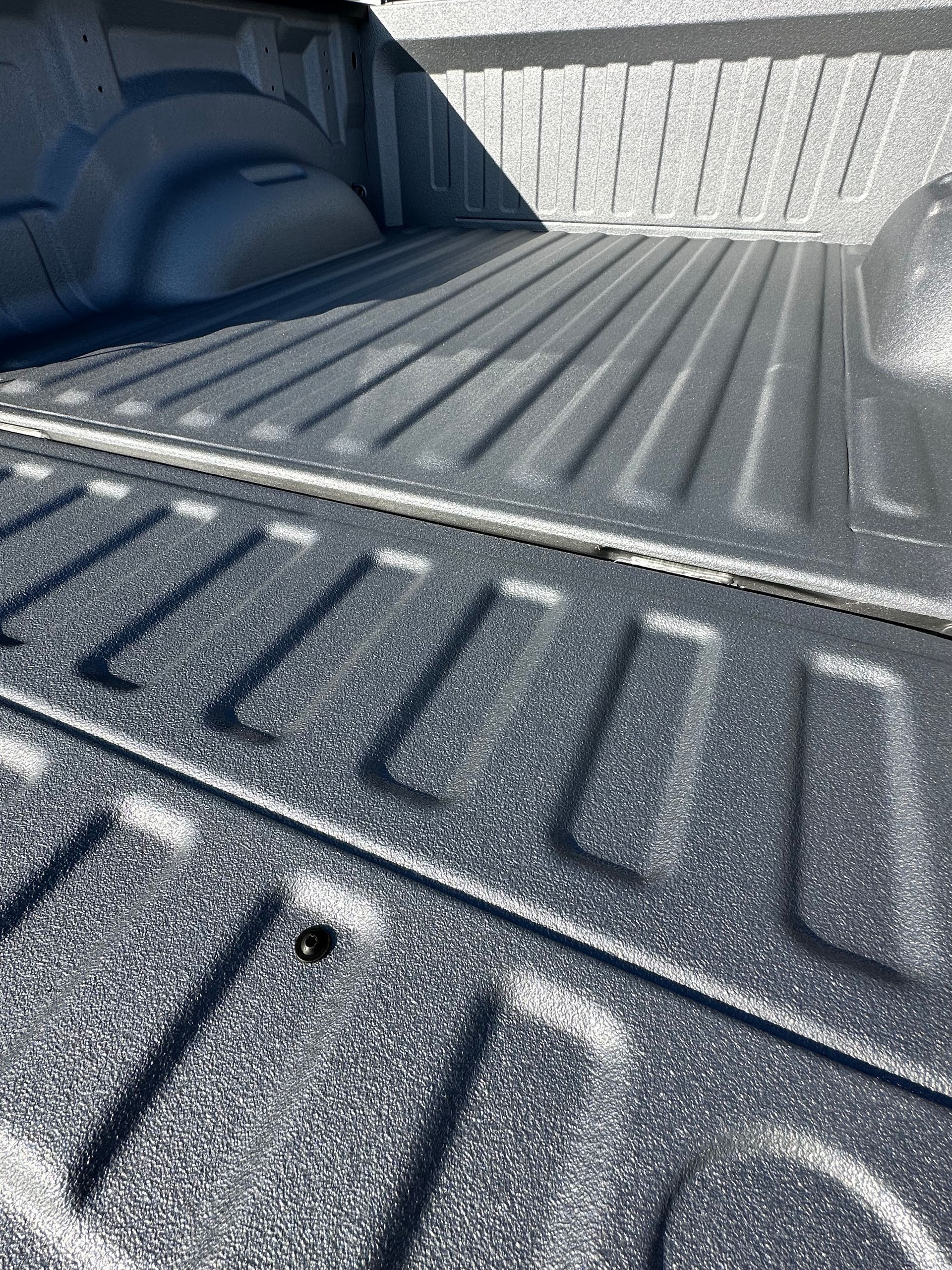 A truck bed with a textured black spray-in liner, showing a corrugated floor and side walls in daylight.