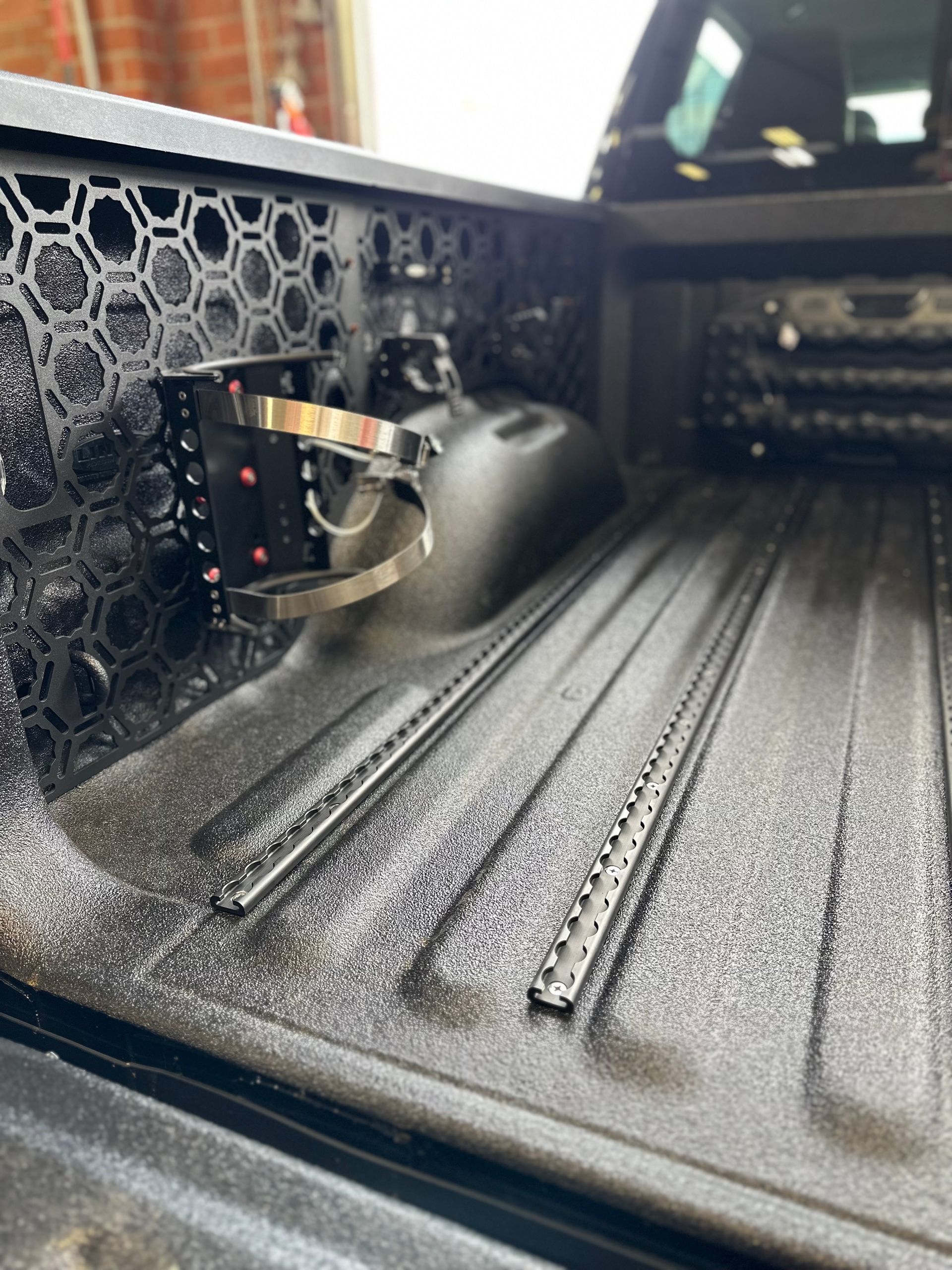 A pickup truck bed featuring a black hexagonal modular storage panel mounted on the side with a metal fire extinguisher mount.