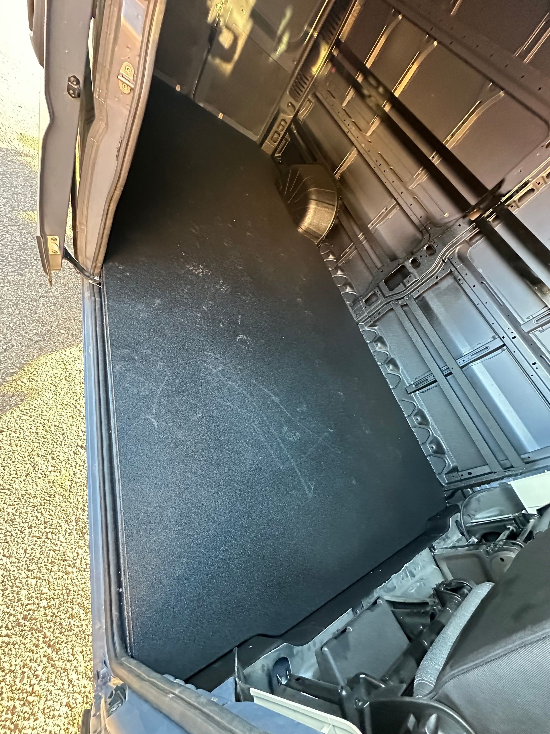 A view inside a vehicle with a dark, textured floor mat covering the cargo area, next to metal ribbed interior walls.
