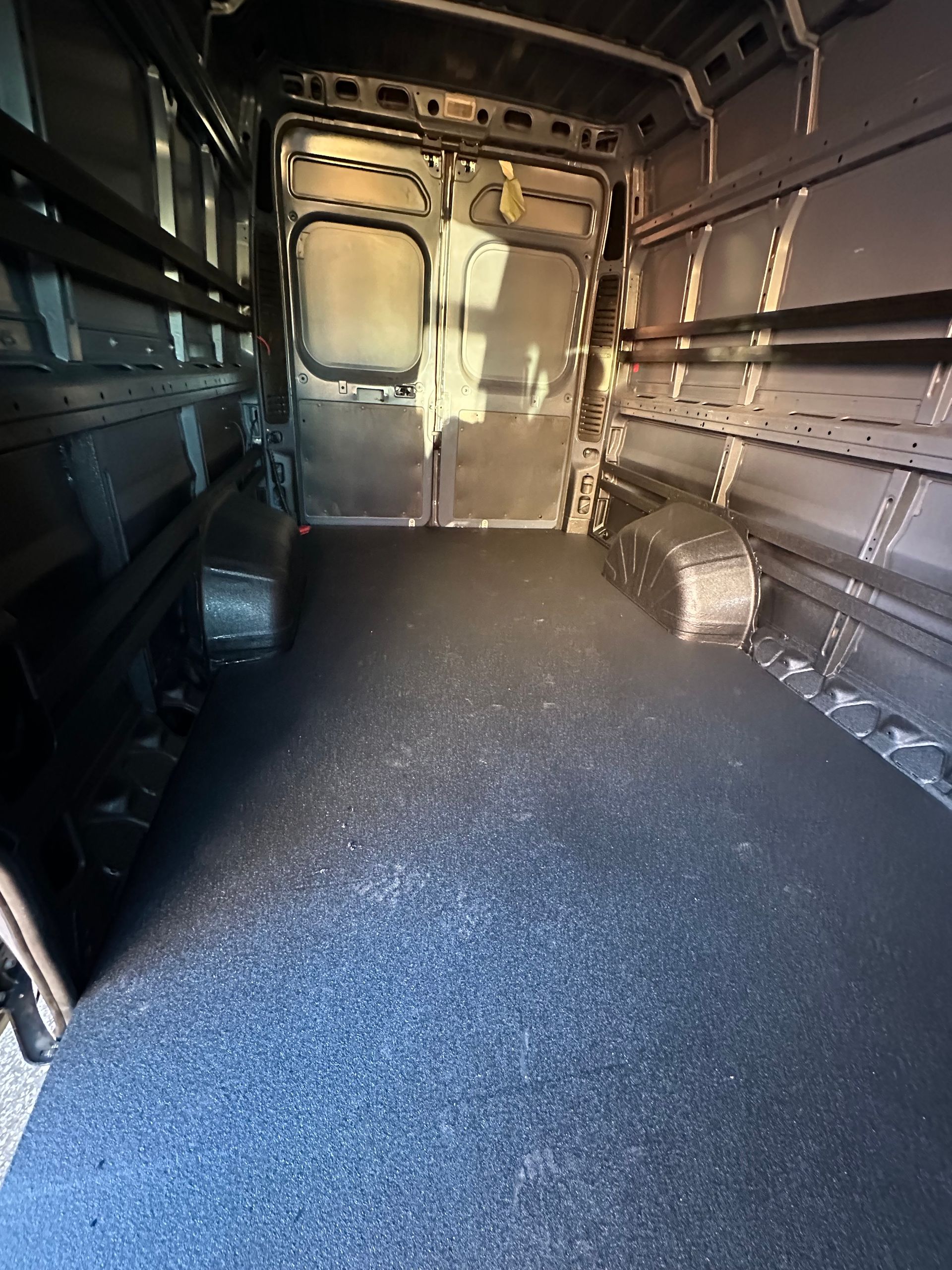Inside of an empty cargo van with dark grey textured flooring and metal walls.
