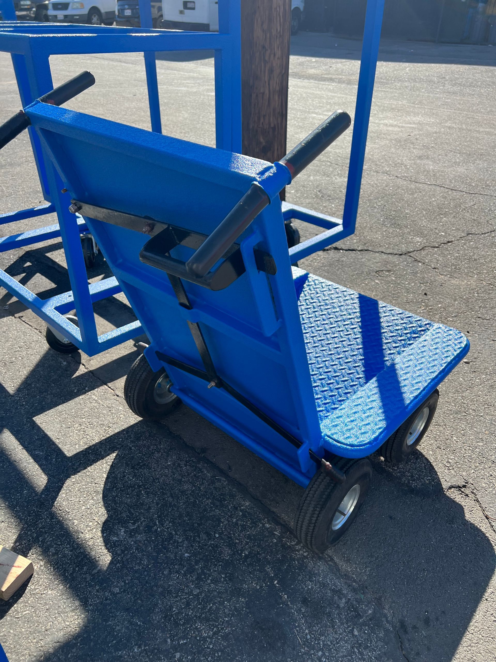 A blue industrial utility cart with two handles and small wheels, parked on asphalt outdoors.