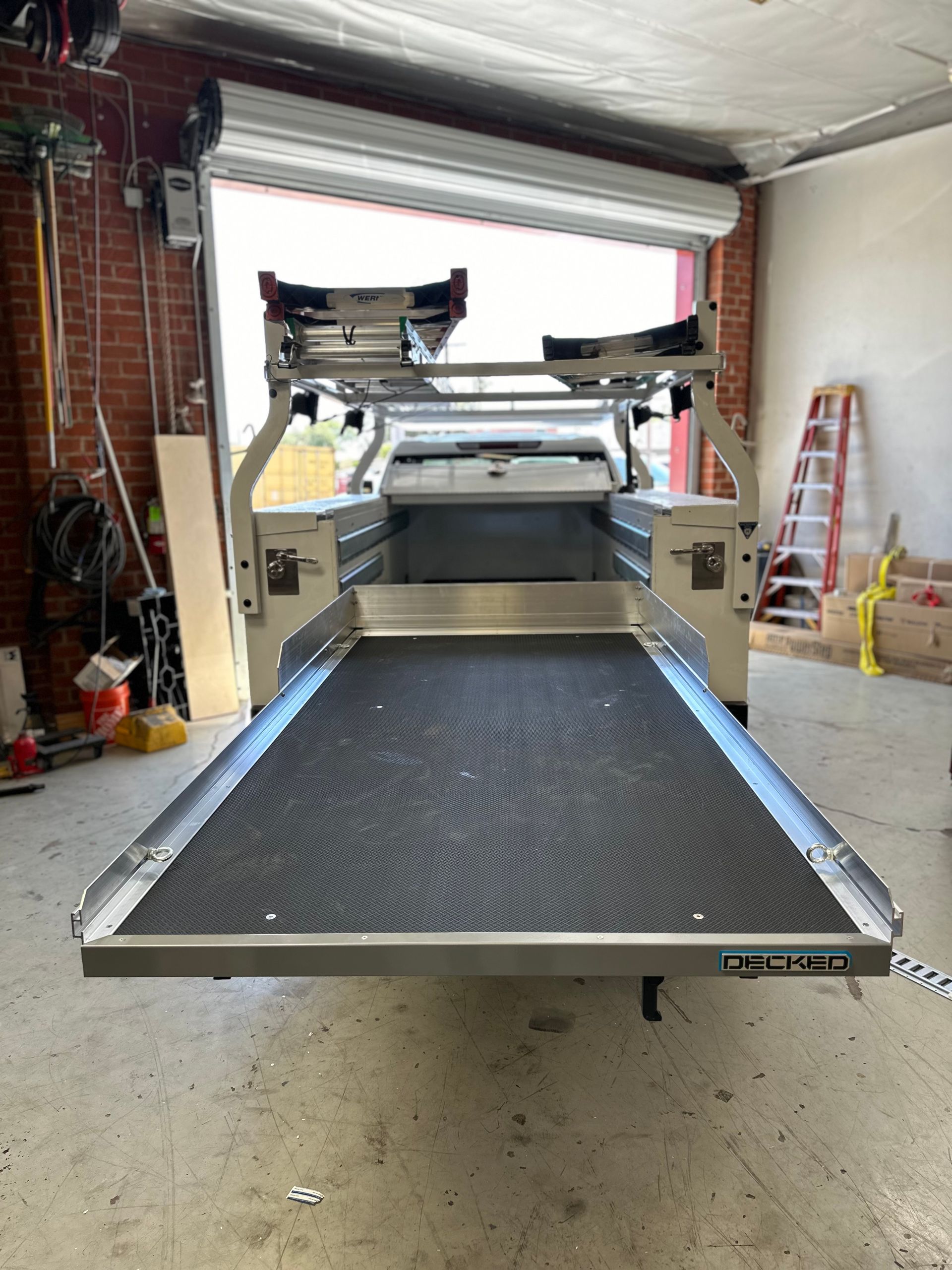 A sliding metal cargo tray for a truck bed is extended outward inside a garage workshop.