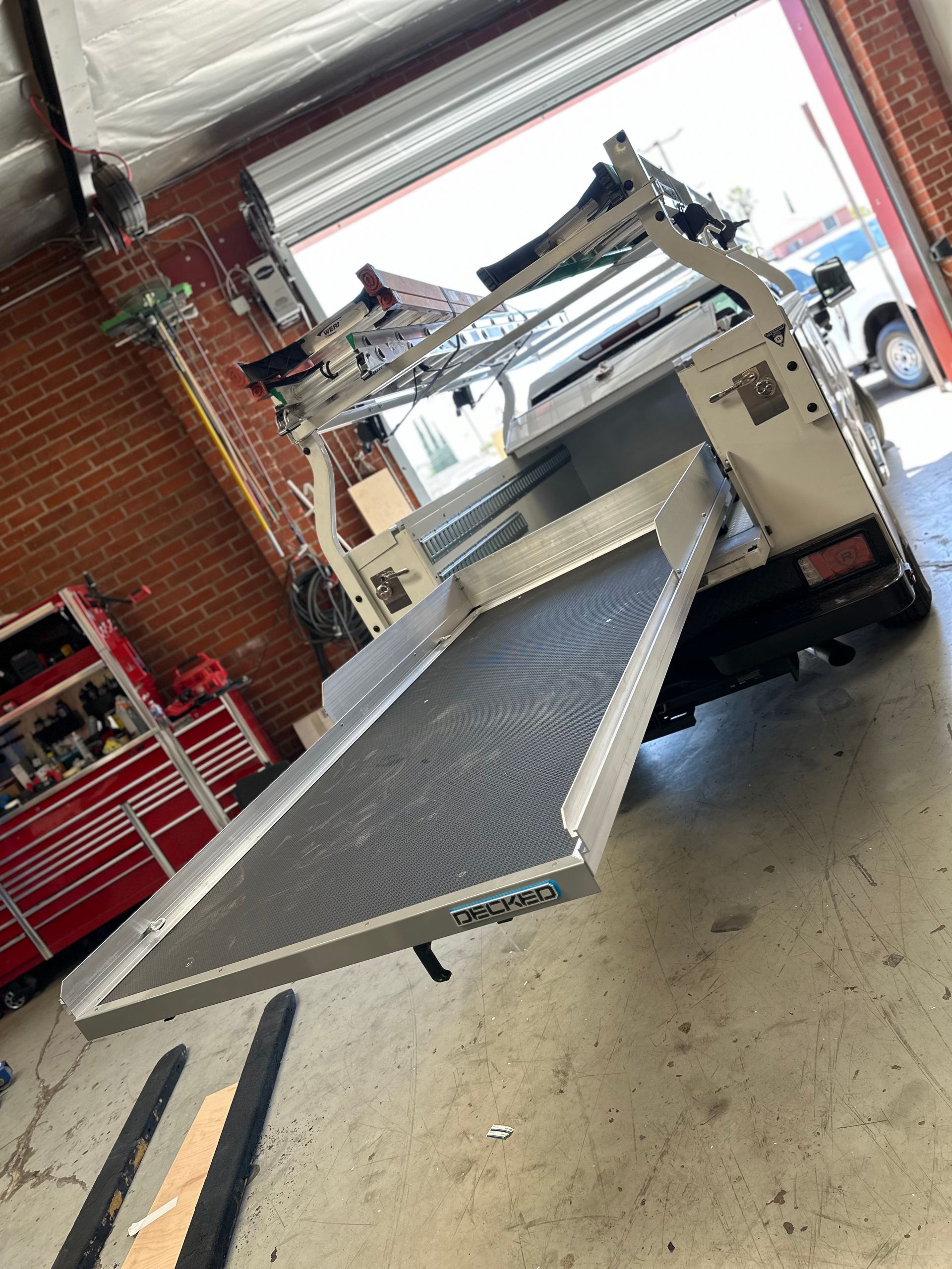 A metal sliding truck bed cargo tray extended outward from the back of a utility truck in an auto shop.