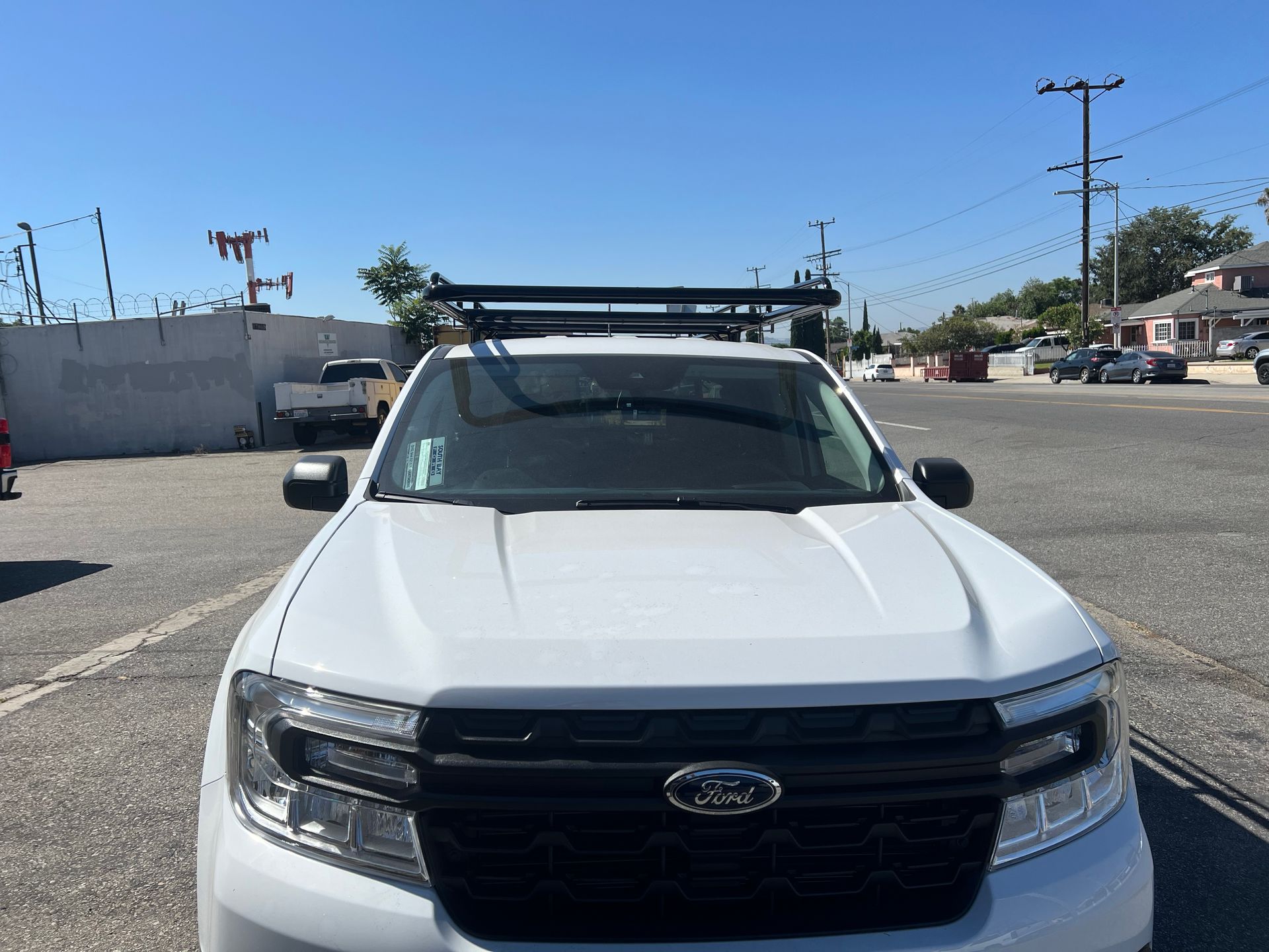 A front view of a white Ford pickup truck with a black roof rack, parked in a paved outdoor lot on a sunny day.