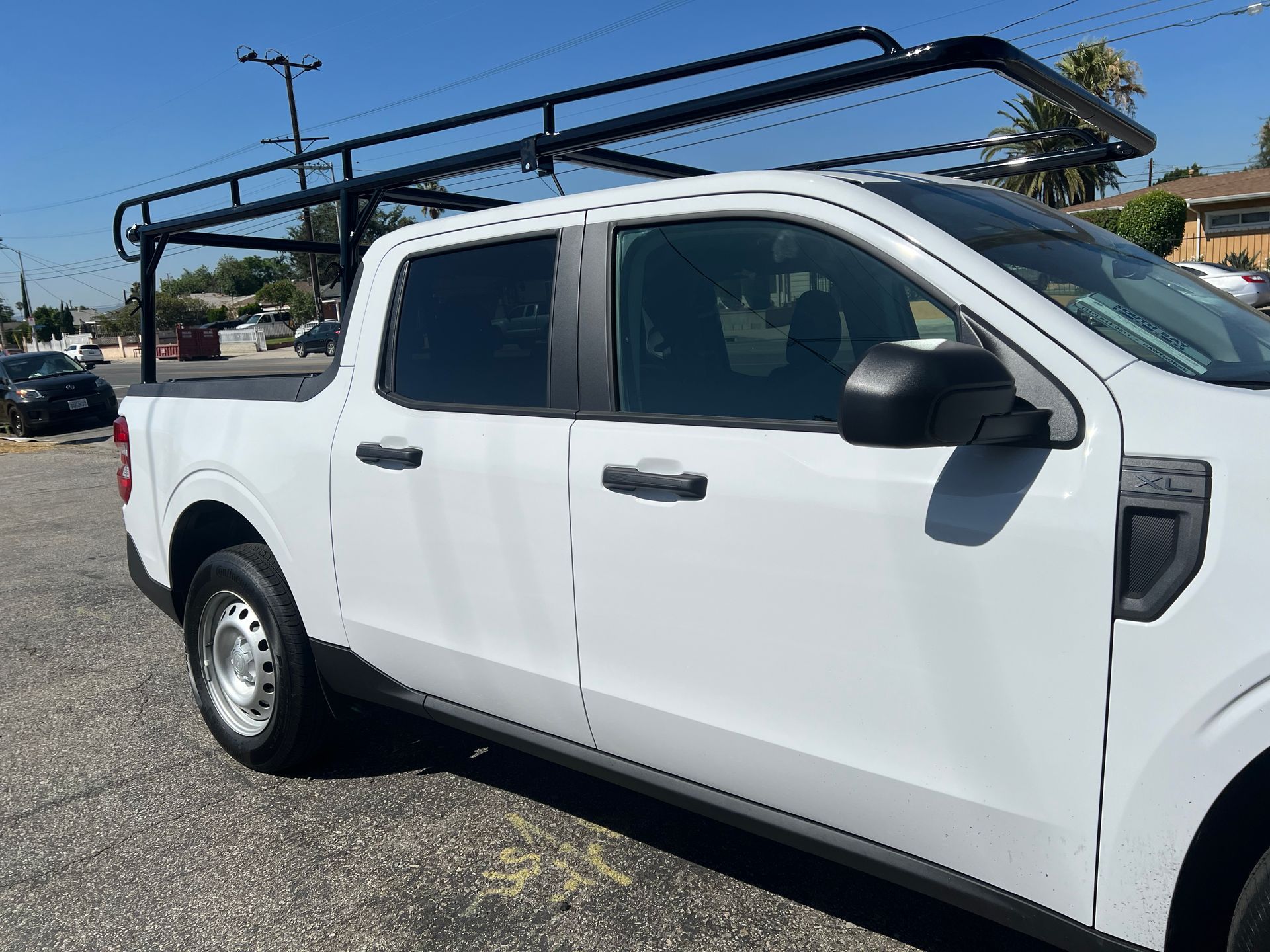 A white pickup truck with a black utility rack parked in a lot under a clear blue sky.