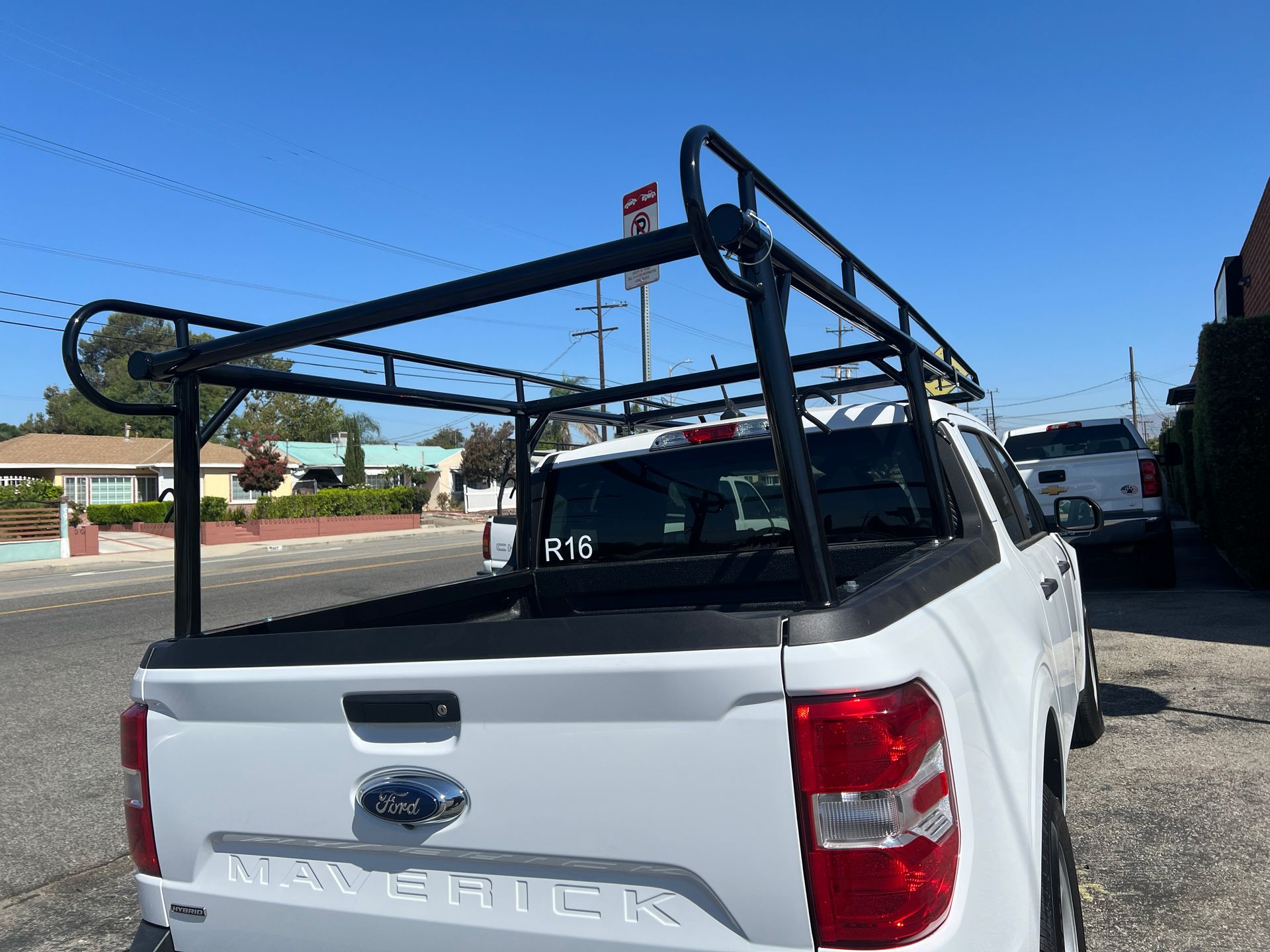 A white Ford Maverick pickup truck parked outdoors, featuring a large, black metal utility ladder rack over the bed.