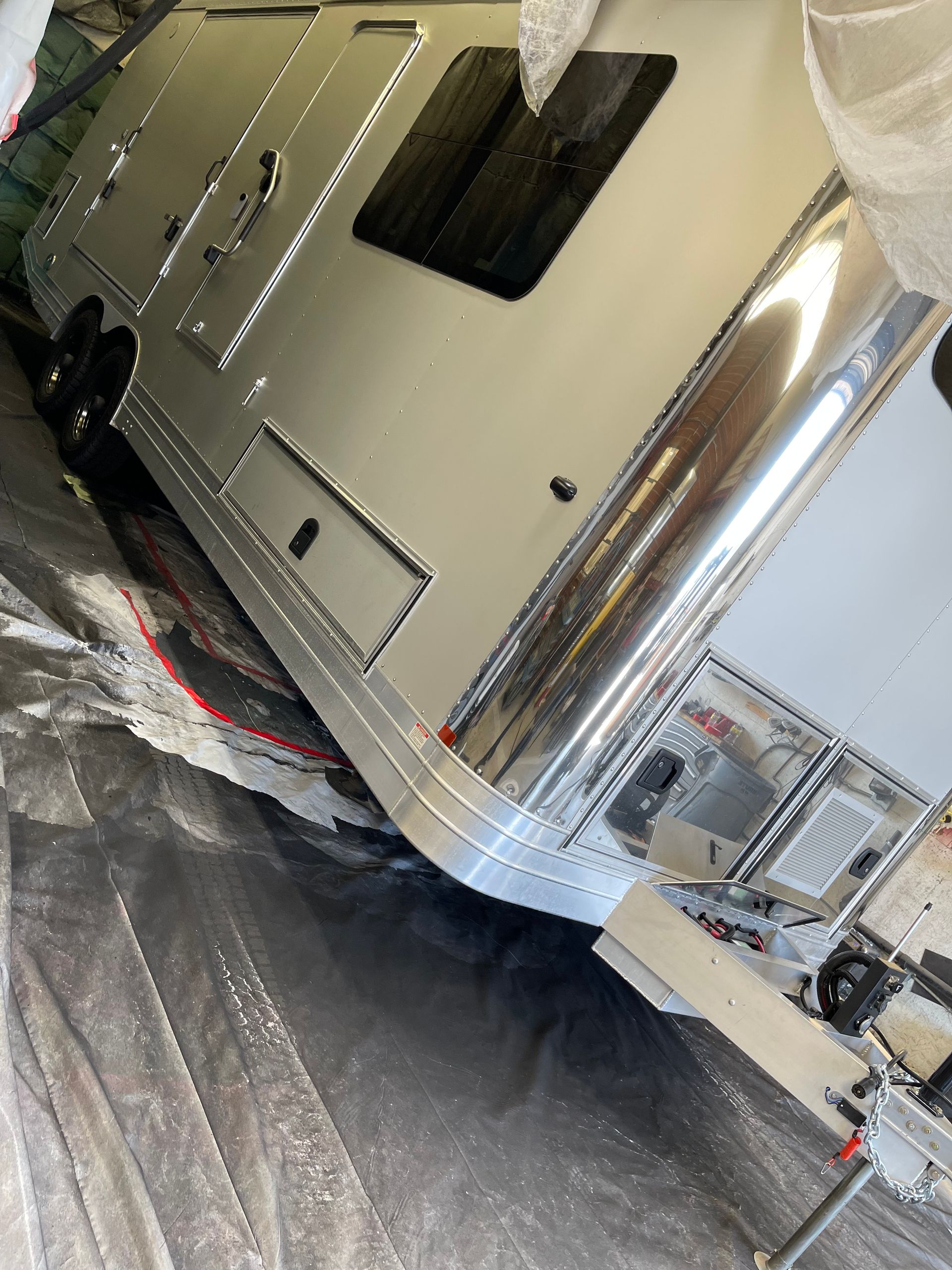 An Airstream trailer with a polished, reflective silver exterior parked on a protective floor covering.
