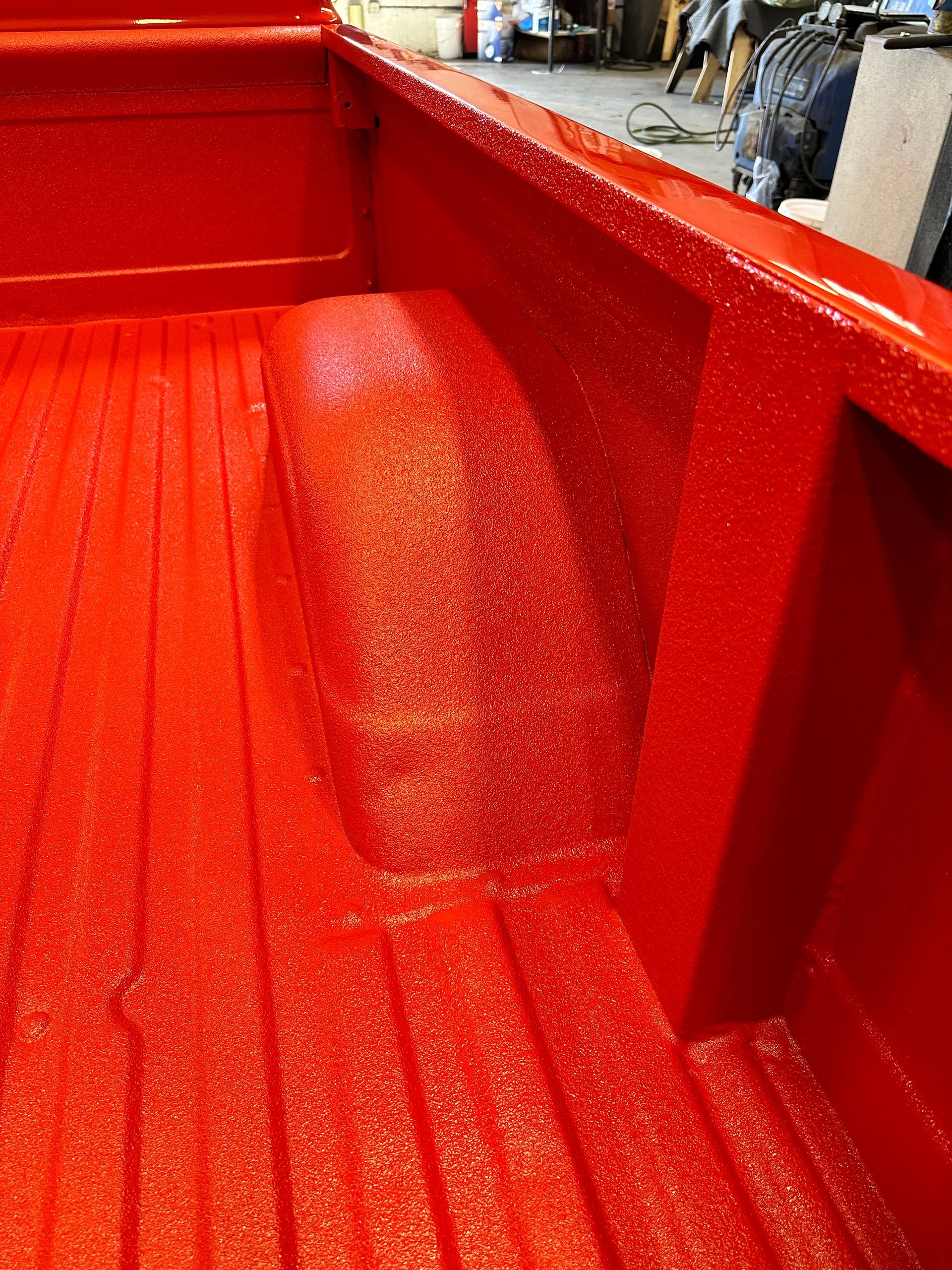 Close-up of a pickup truck bed coated in a bright red, textured protective finish.