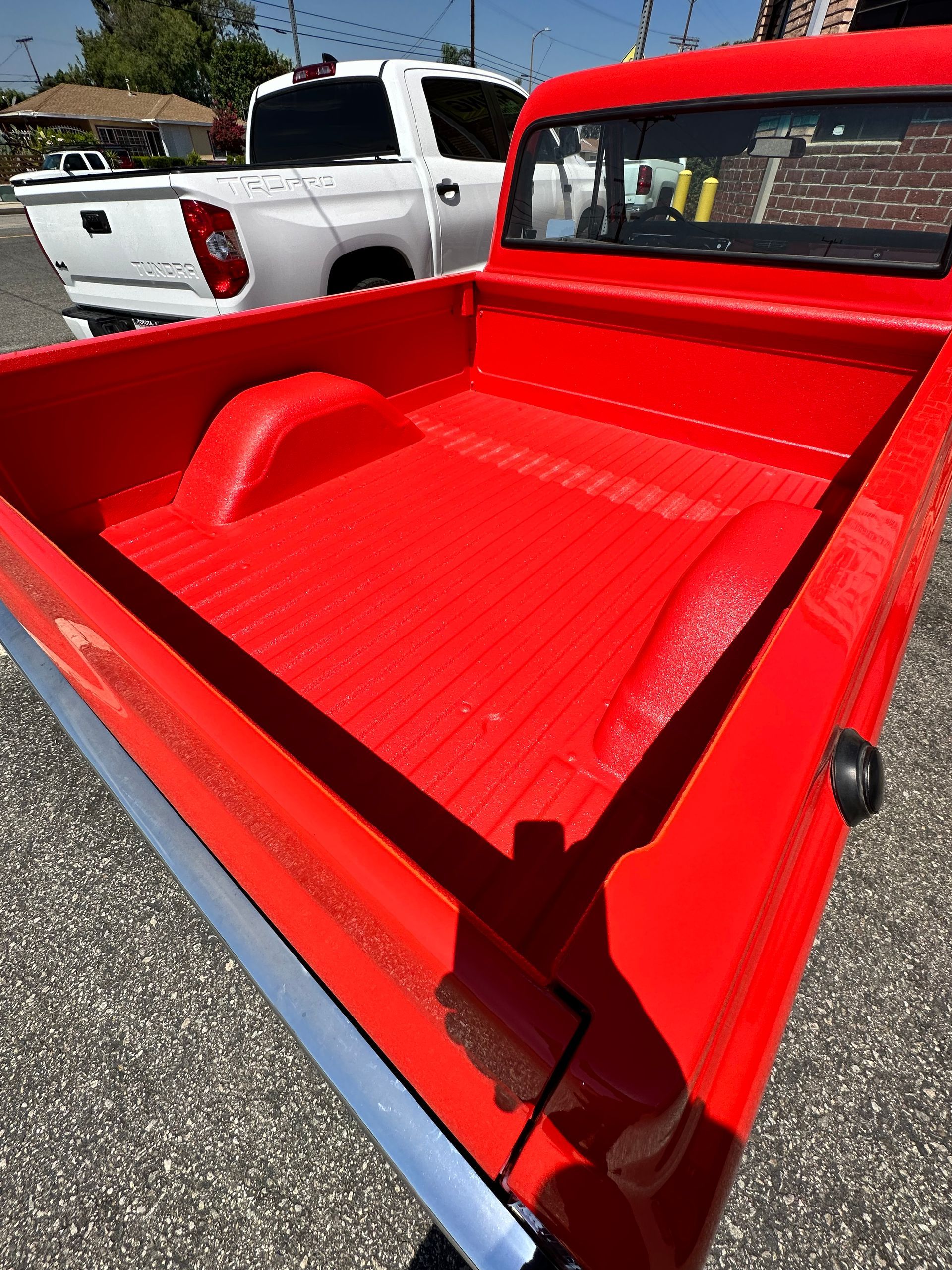 A high-angle view of a bright red truck bed with a textured coating, parked next to a white pickup truck.